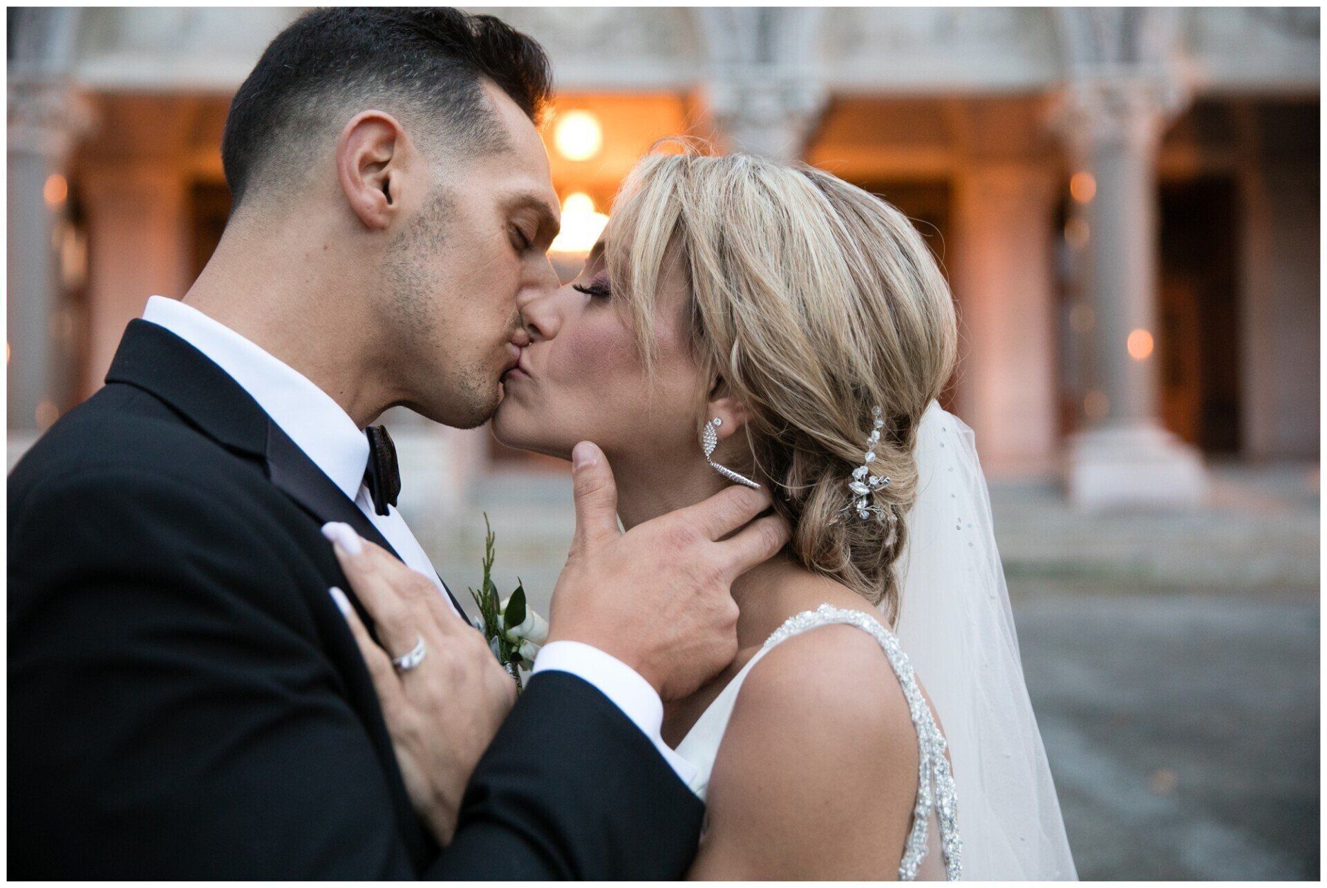 Bride and groom kissing at an outdoor wedding venue, with warm lights in the background