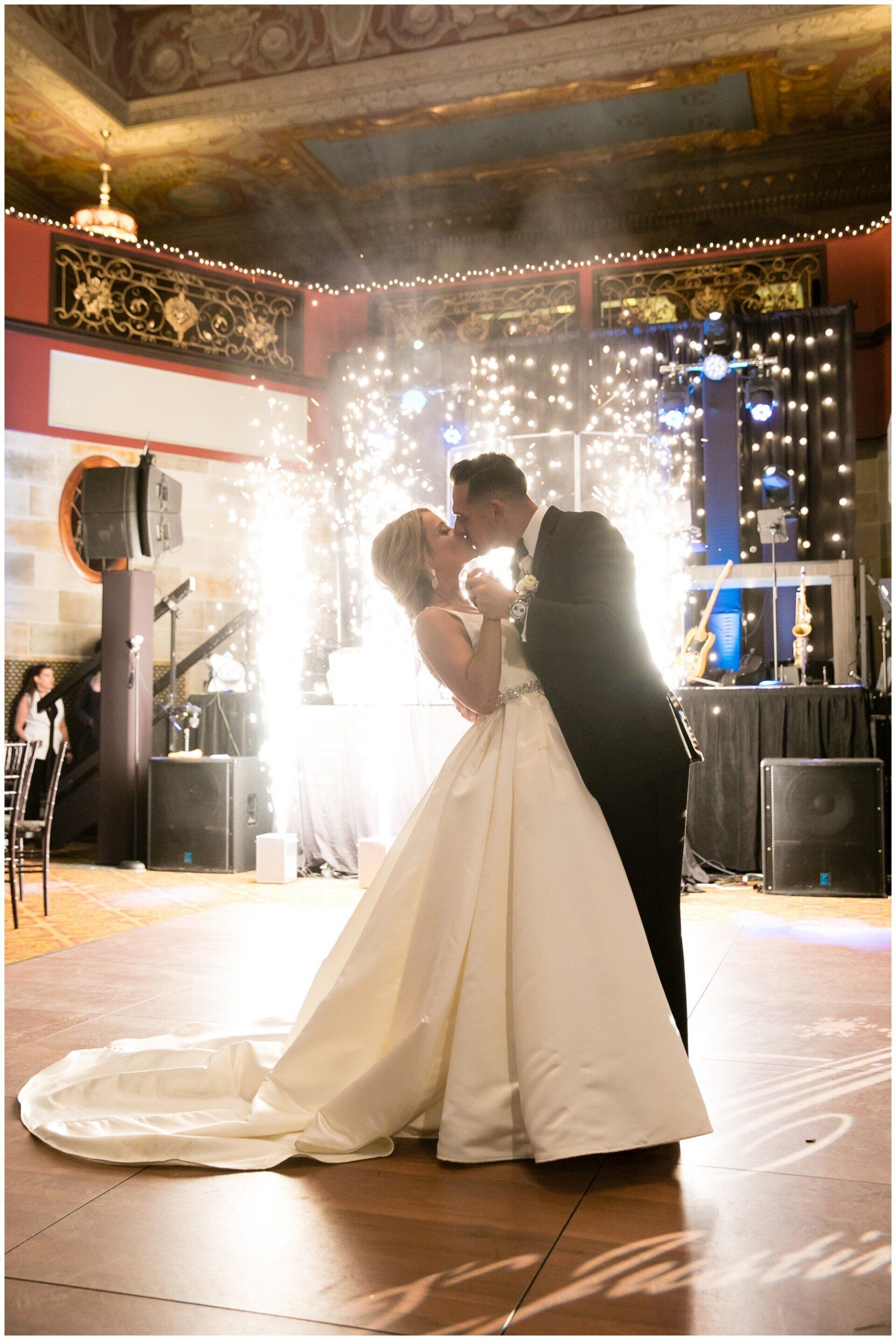 Bride and groom sharing a kiss during their wedding reception, with a bright sparkler backdrop