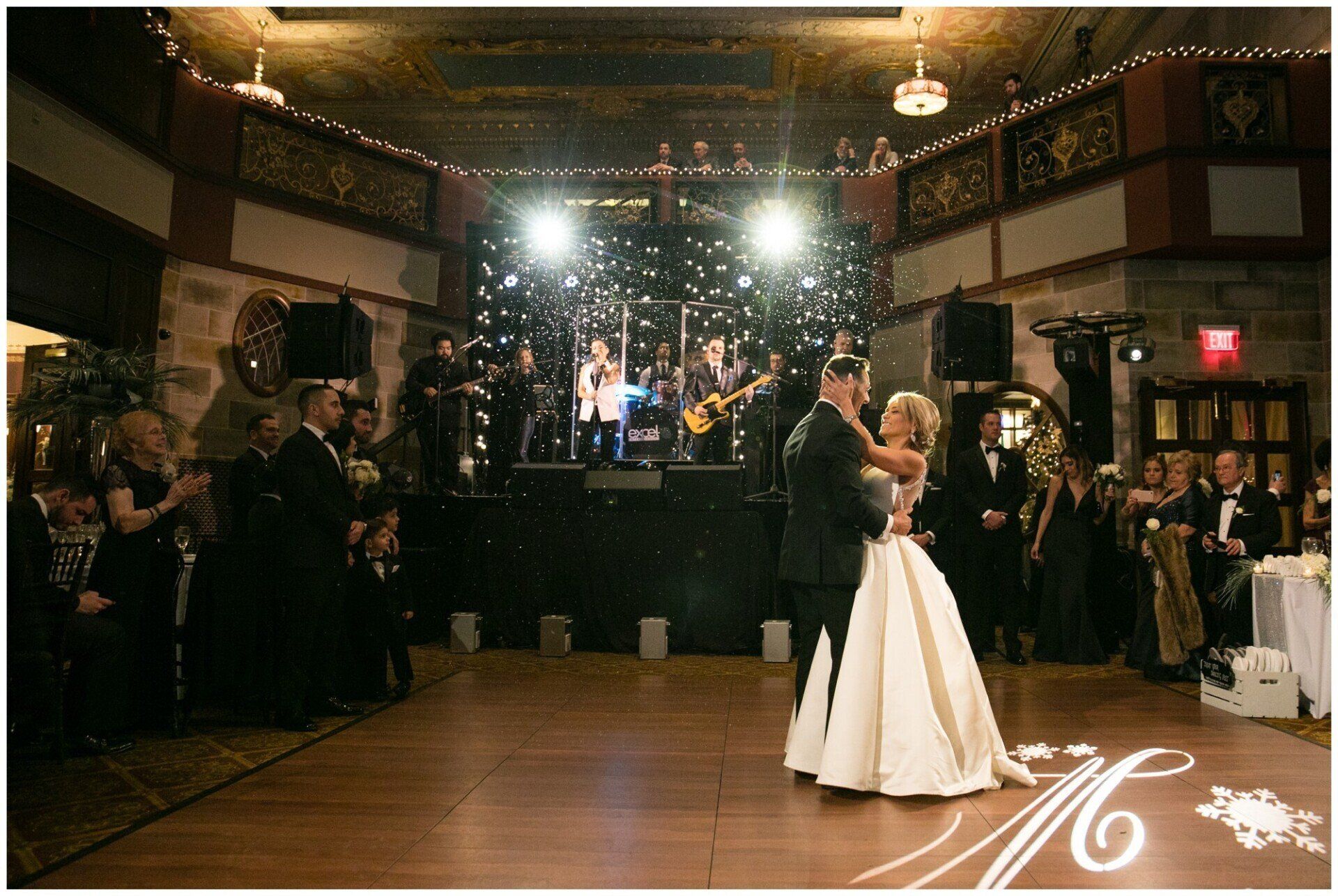Wedding couple dancing in a reception hall with guests watching and a live band on stage