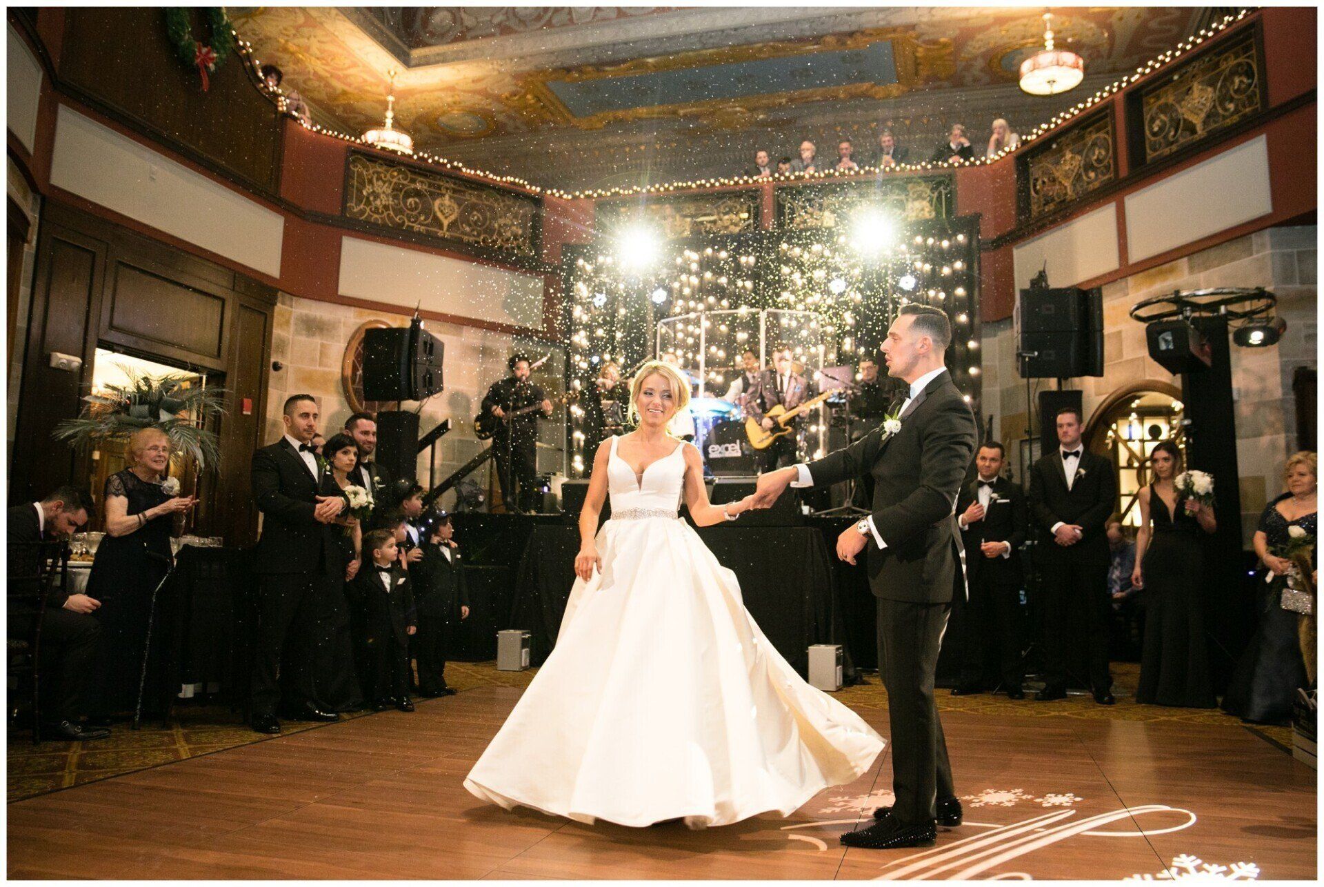 Bride and groom dancing at a wedding reception with guests watching under bright lights