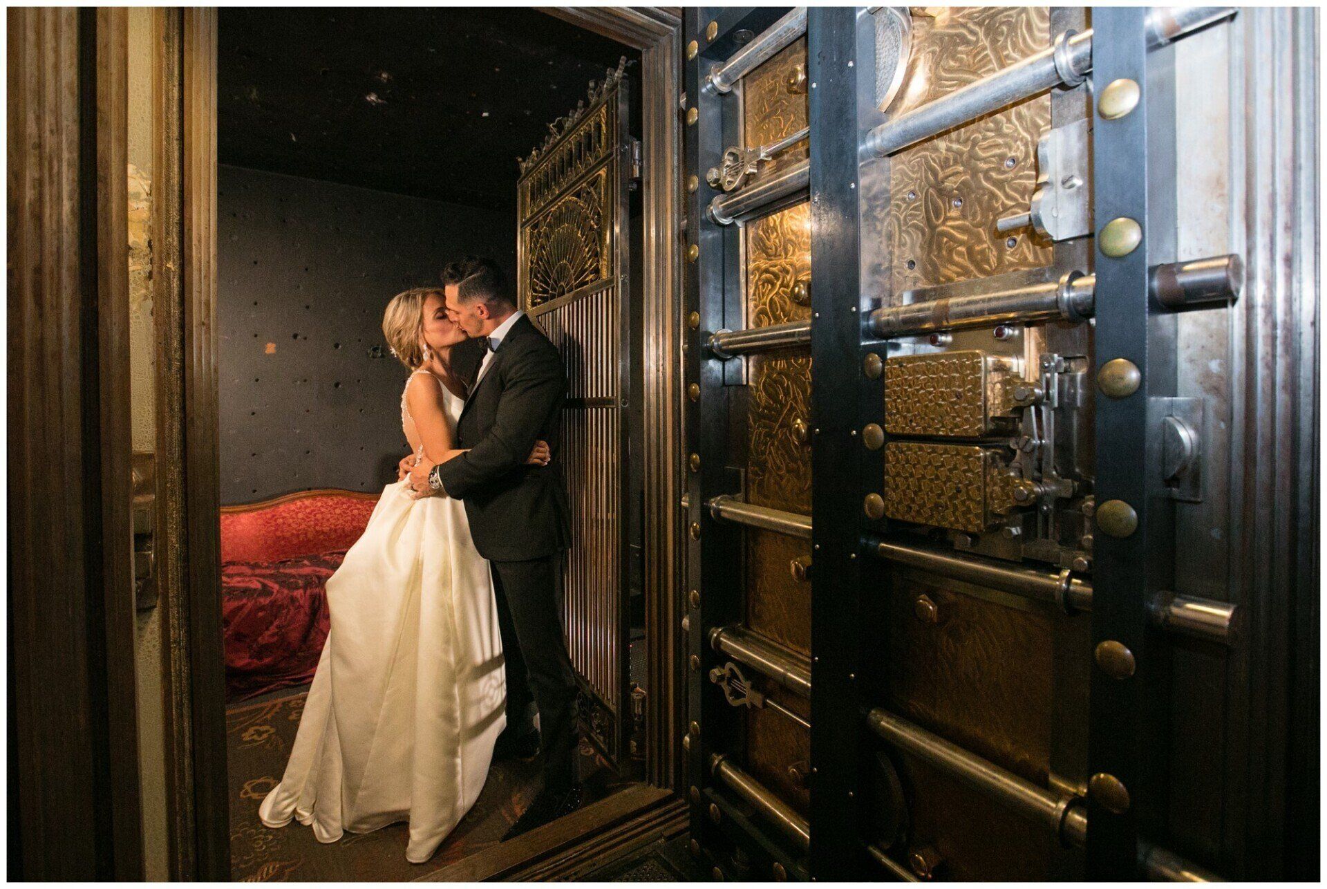 Couple kissing in a doorway beside an ornate metal vault door