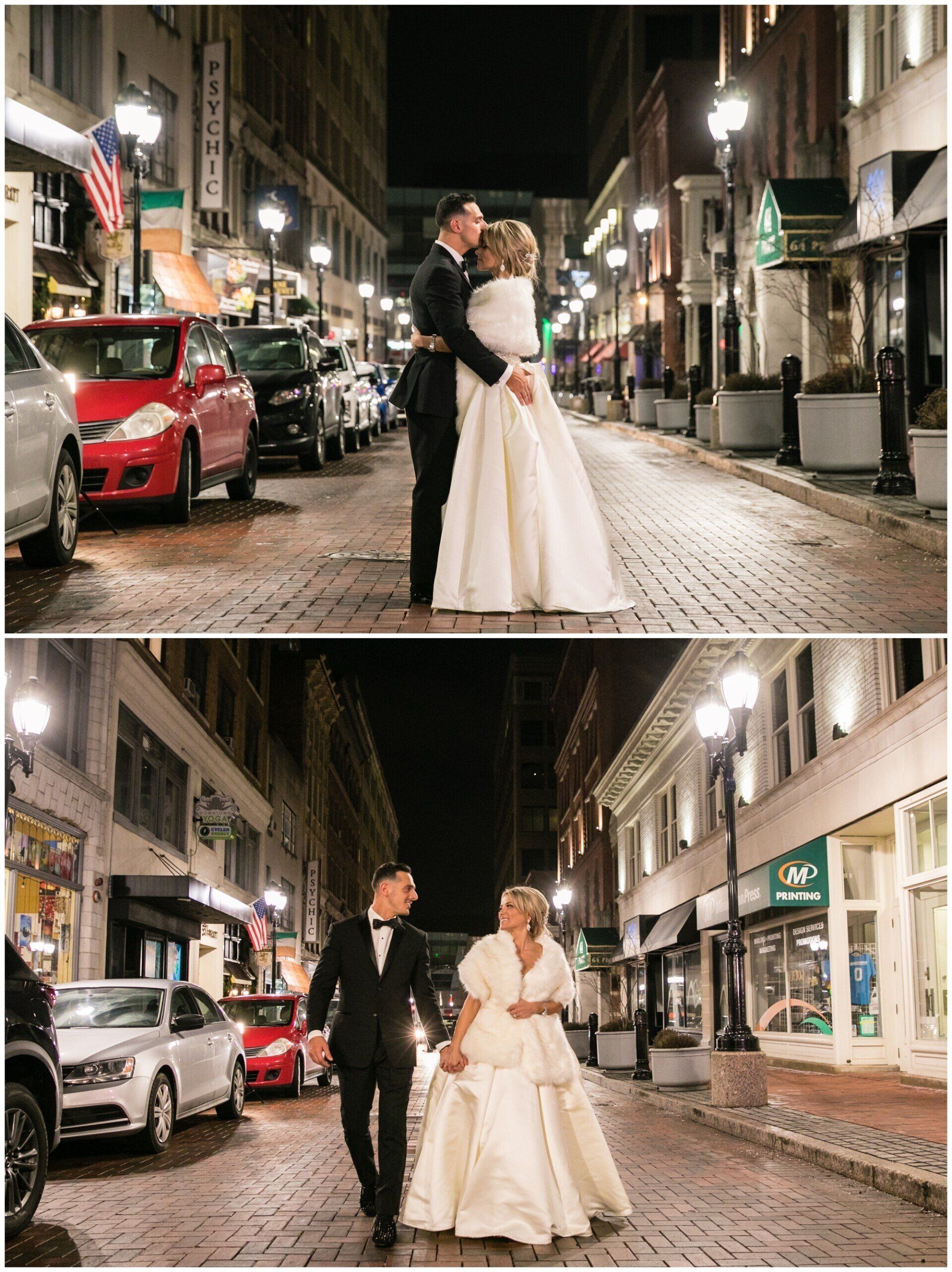 Bride and groom embrace on a wet city street at night, then walk hand in hand between parked cars.