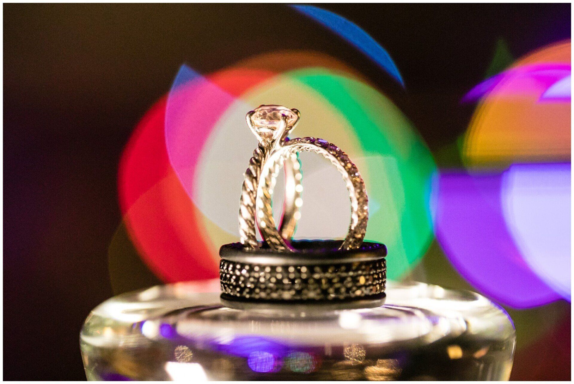 Two gold rings on a glass surface with colorful blurred lights in the background
