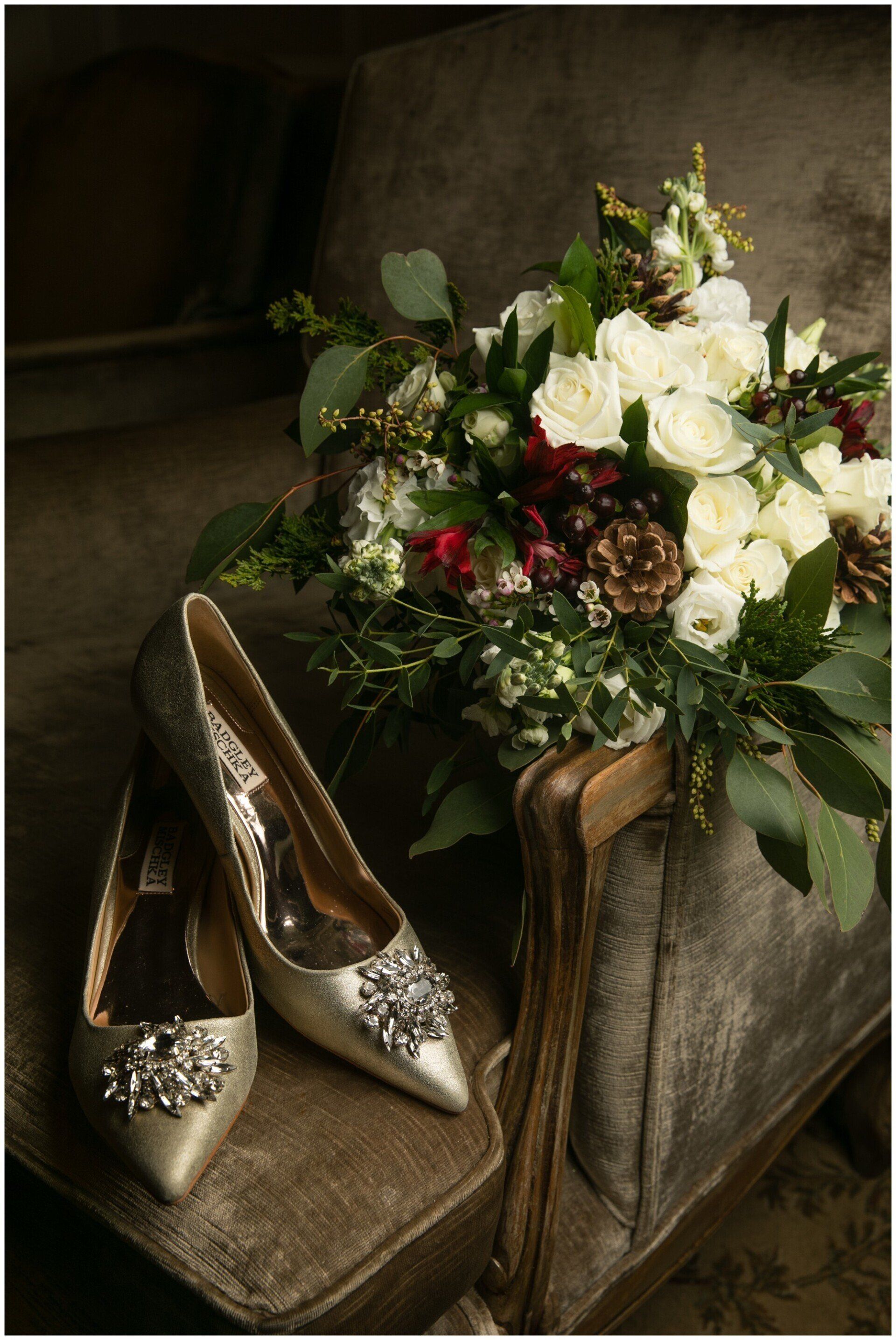 Silver heels beside a bouquet of white and dark flowers on a velvet chair