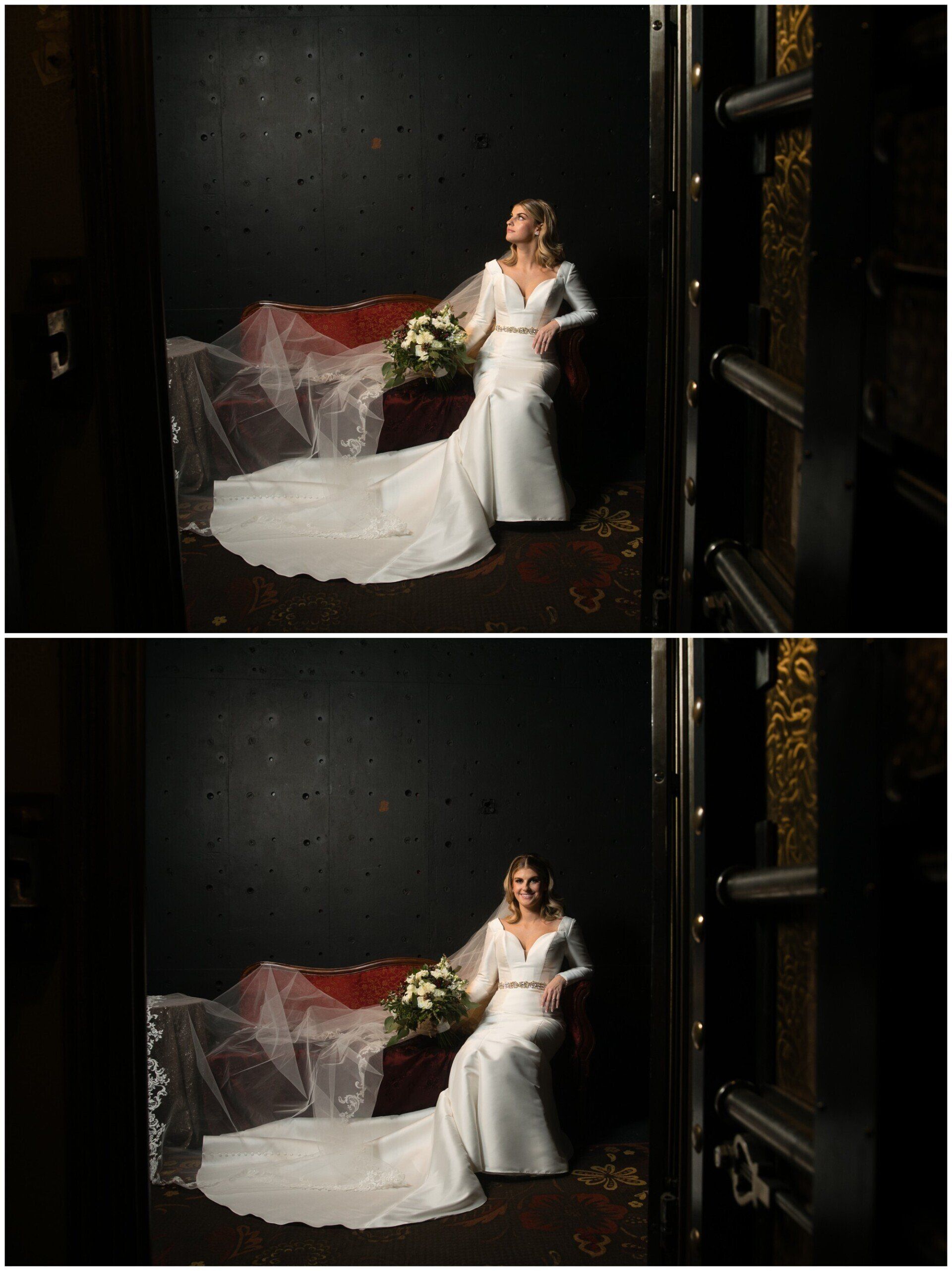Bride in a white gown with a long train, standing beside red flowers against a dark wall.