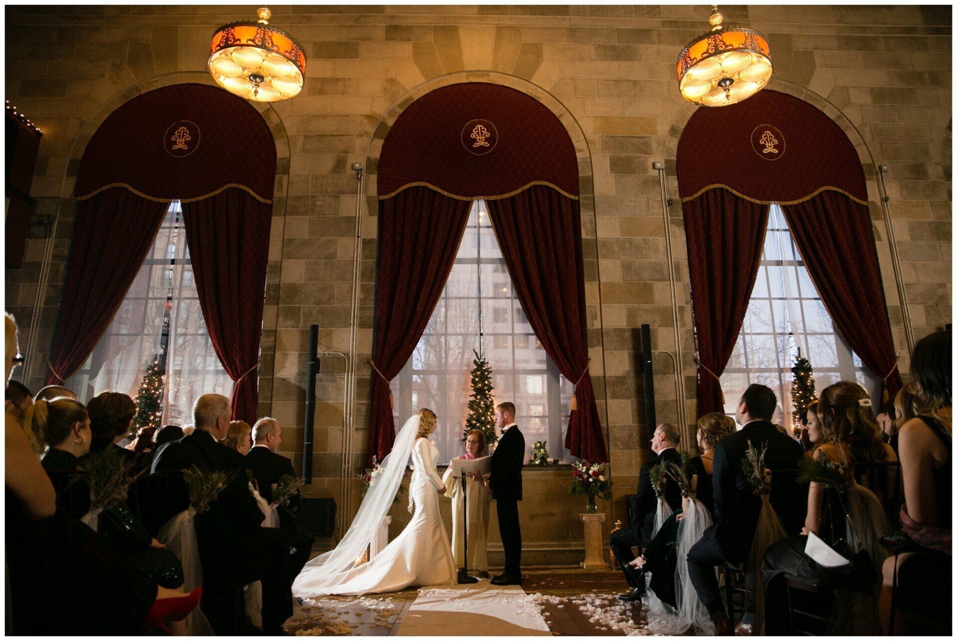 Wedding ceremony in an elegant ballroom with a bride and groom beneath tall red drapes