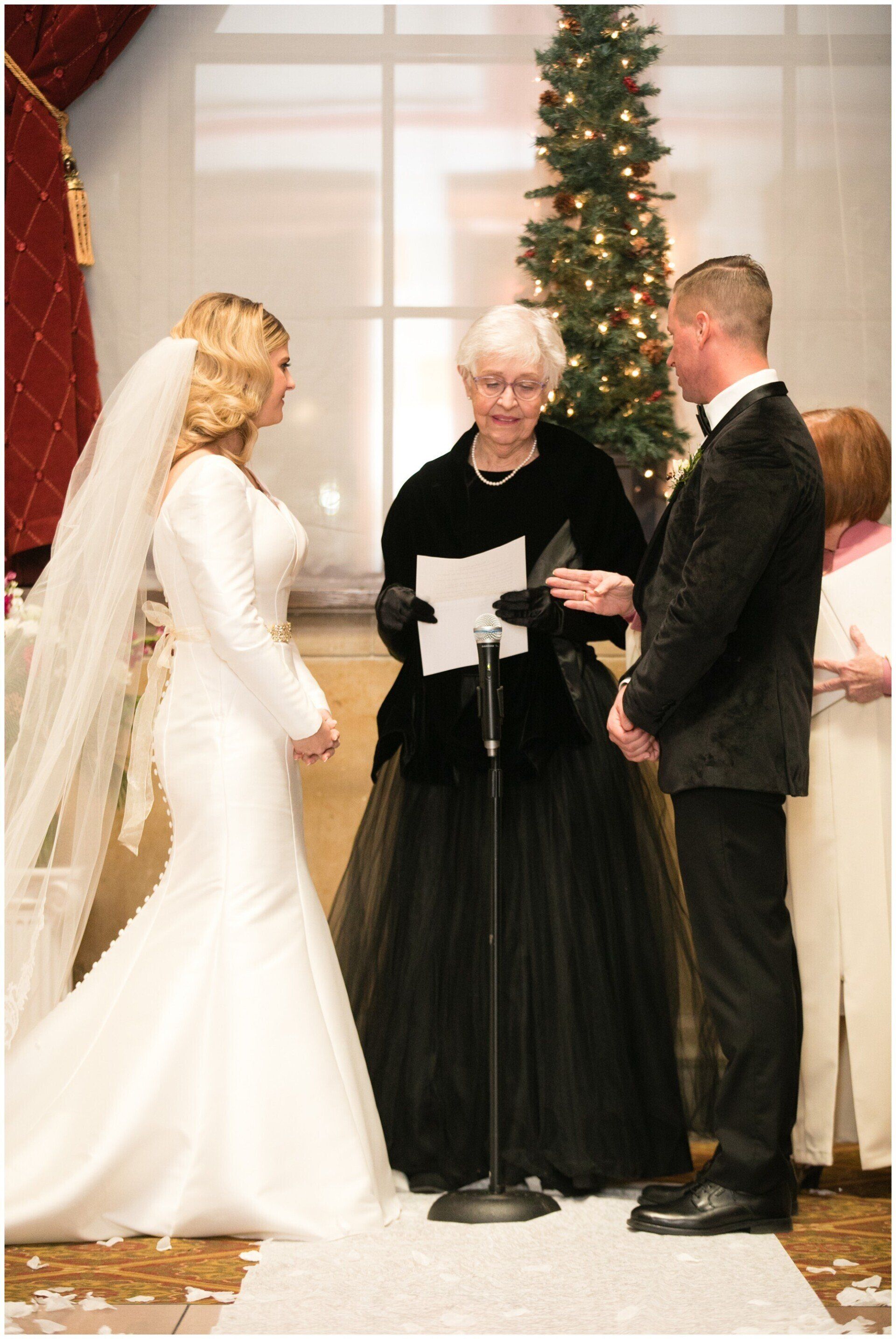 Wedding couple with officiant before a decorated Christmas tree indoors