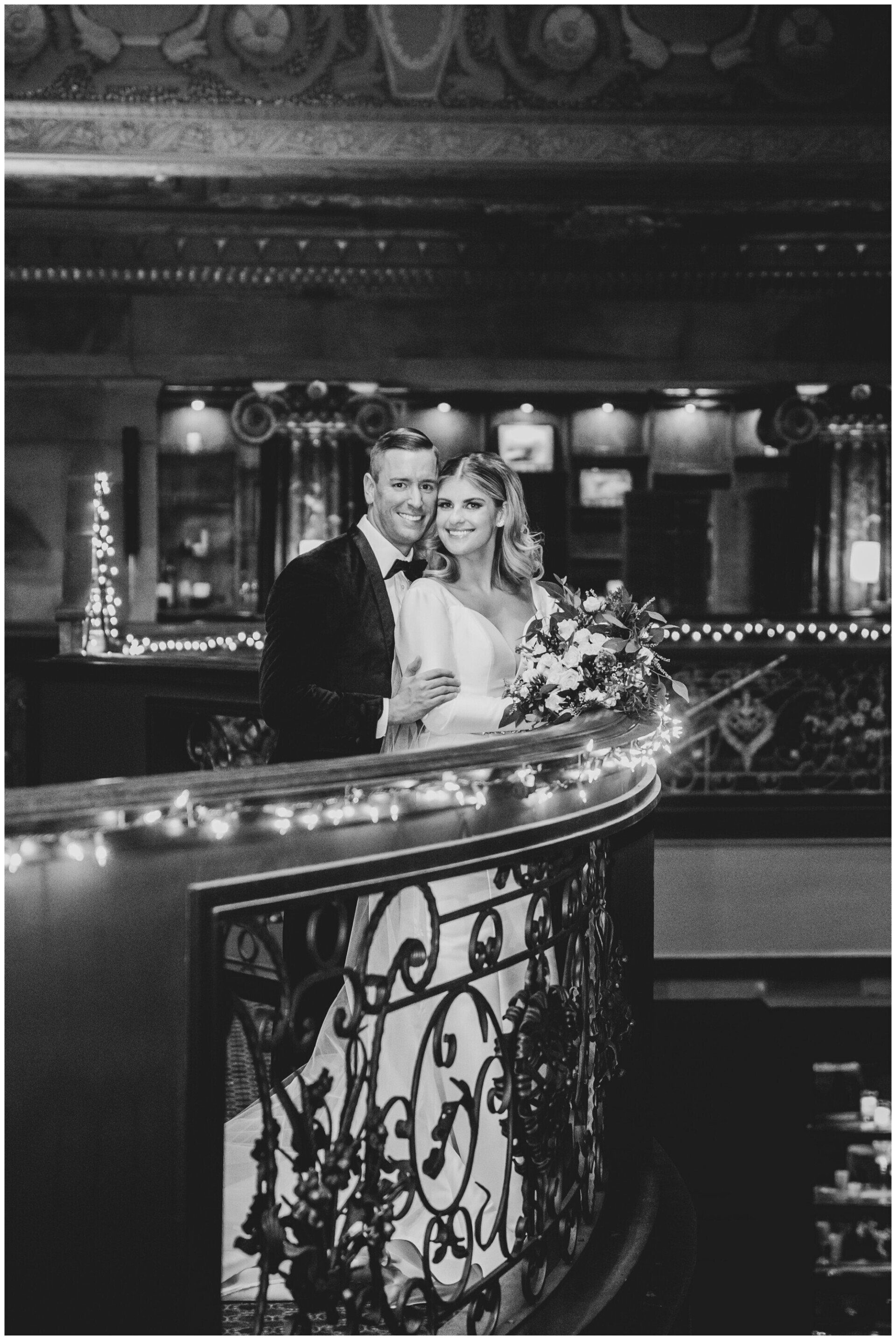 Couple posing behind a decorated balcony in a dimly lit elegant interior