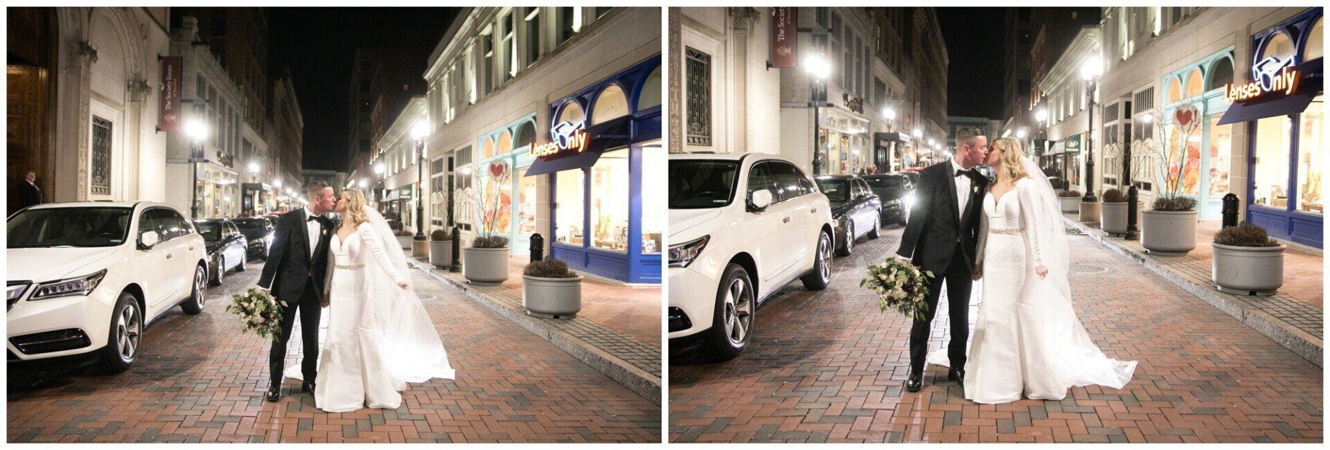 Newlyweds posing on a cobblestone street at night beside parked cars and lit buildings