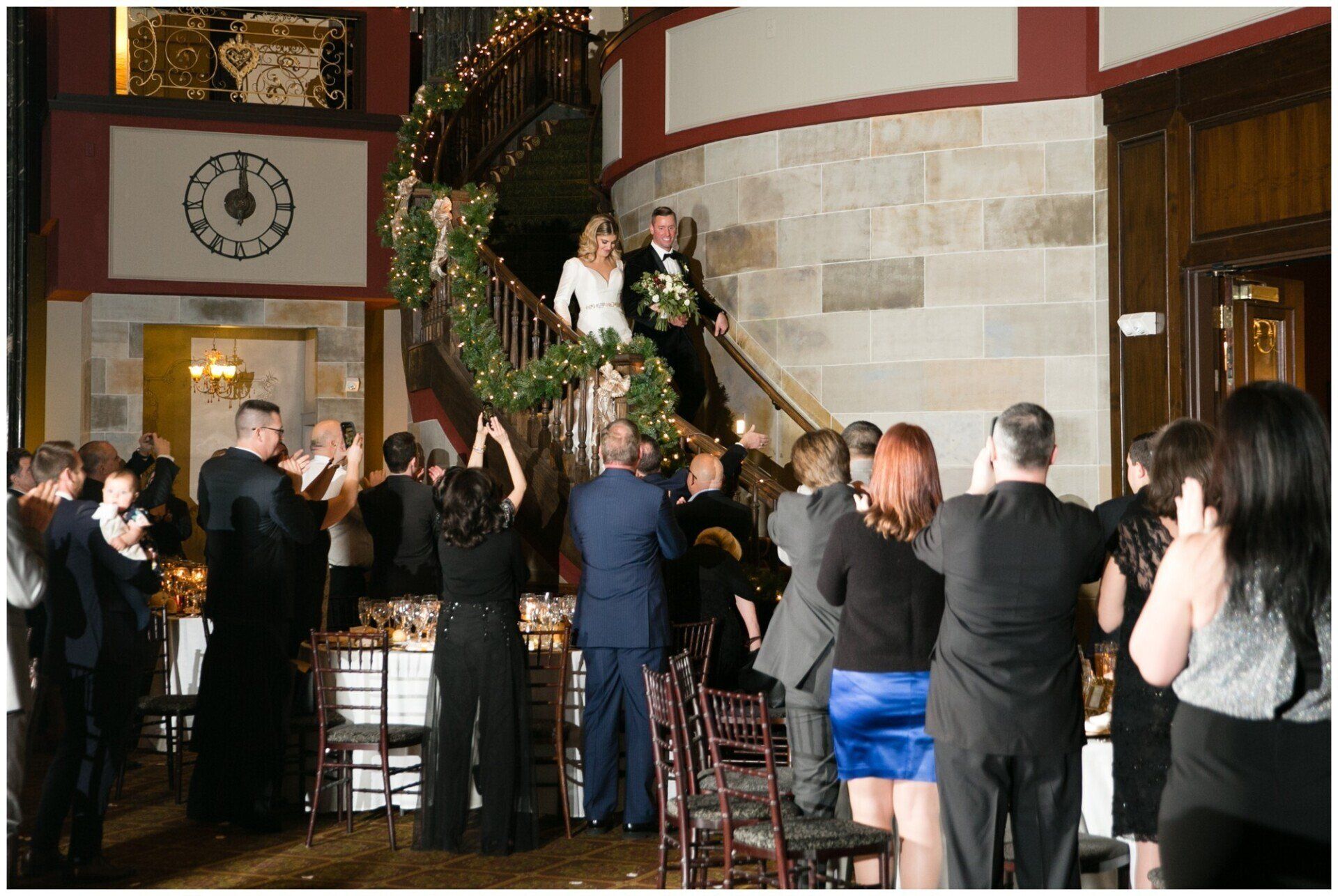 People applauding a newlywed couple on a balcony inside a decorated hall