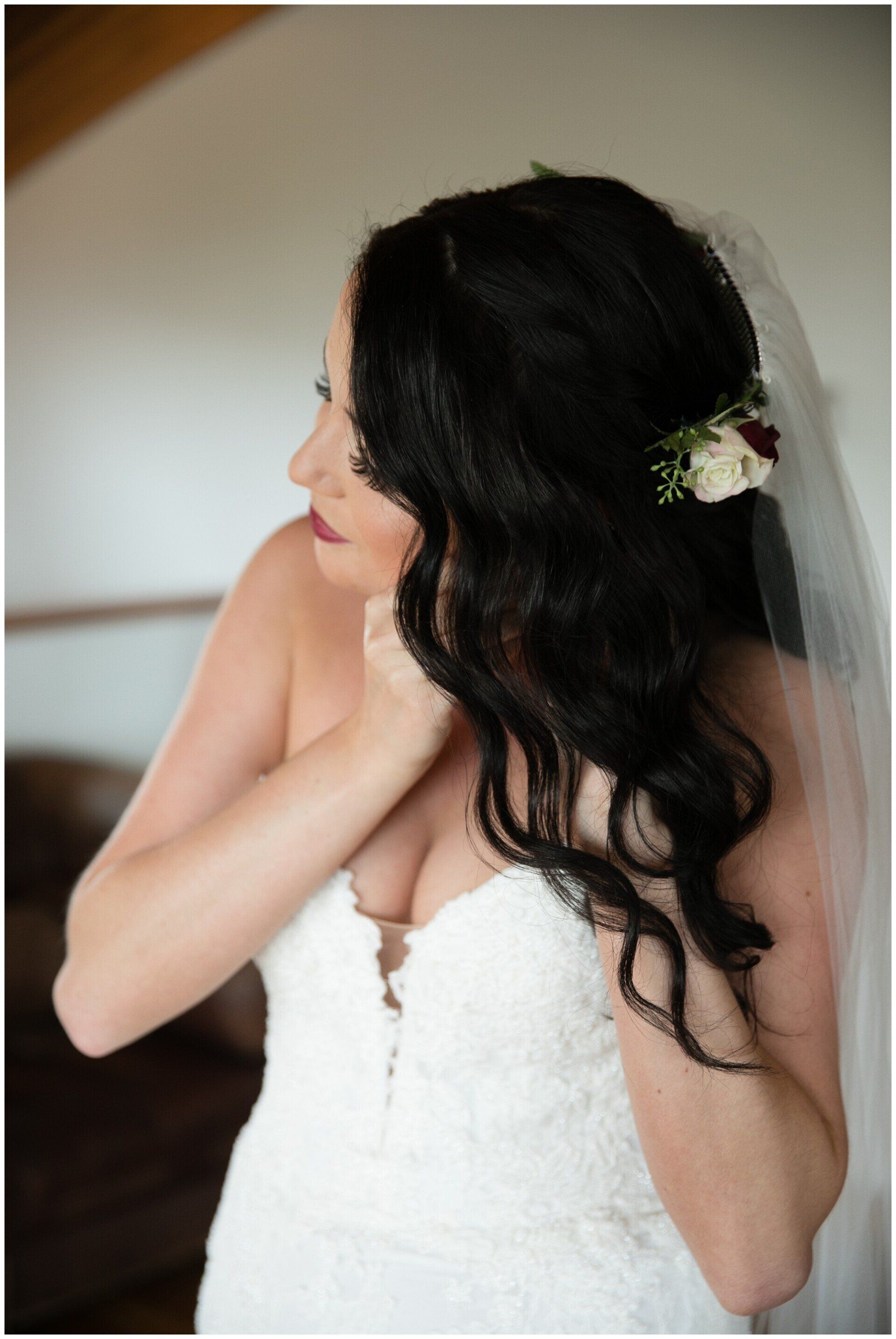 Bride in a white strapless dress adjusting her hair with a veil and white flower accessory.