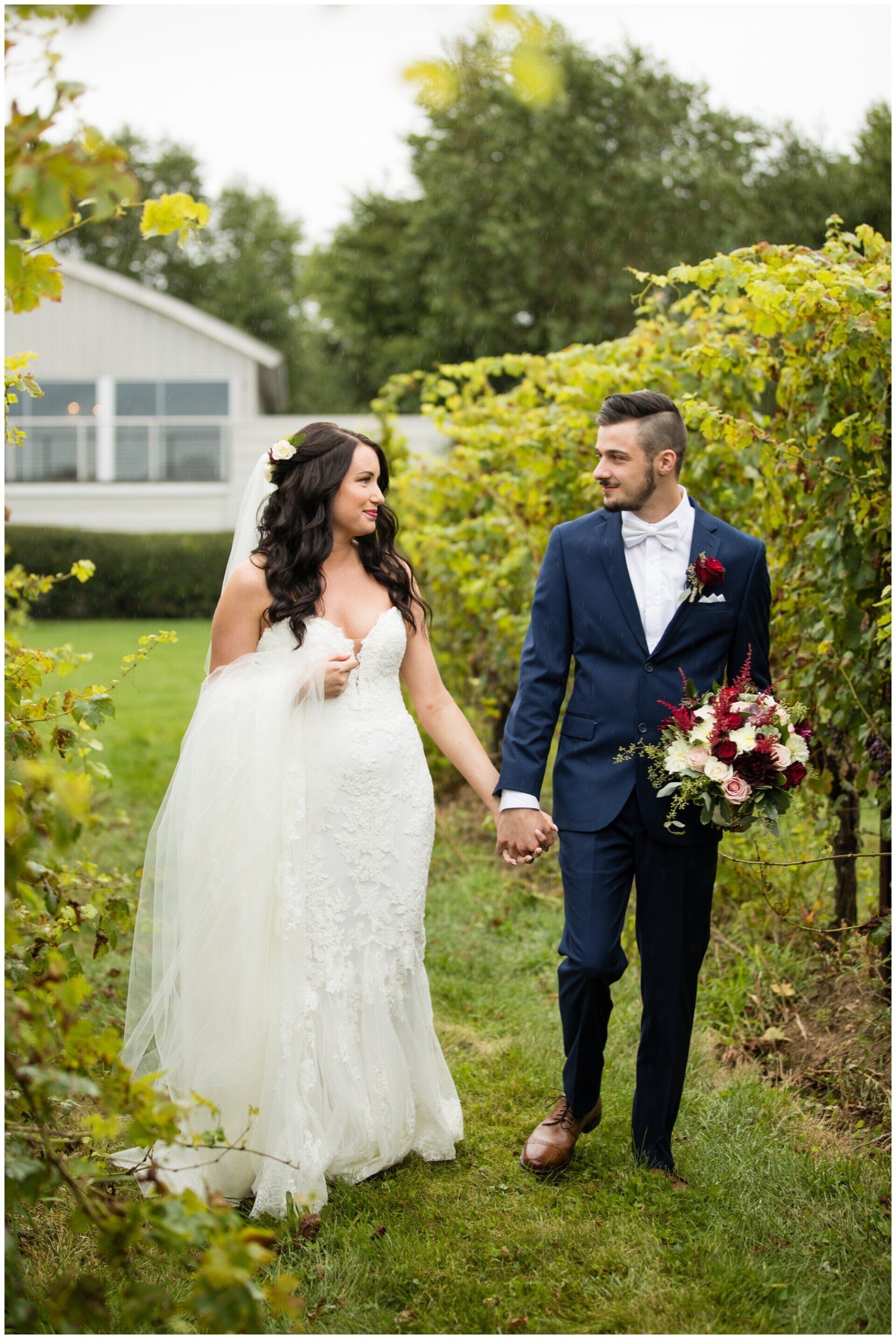 Bride and groom holding hands in a garden, with the groom carrying a bouquet.