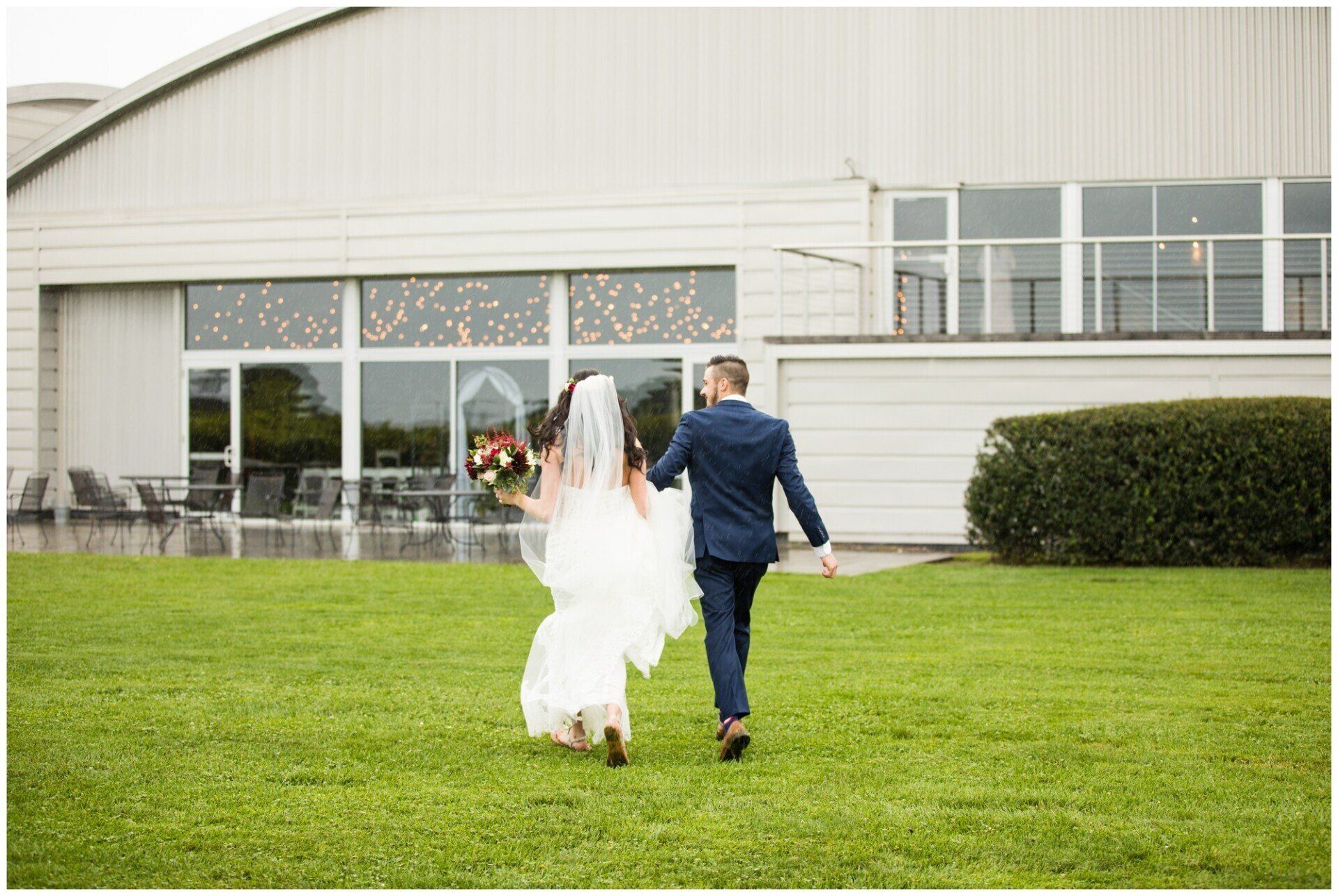 Bride and groom walking hand in hand across a lawn toward a white building