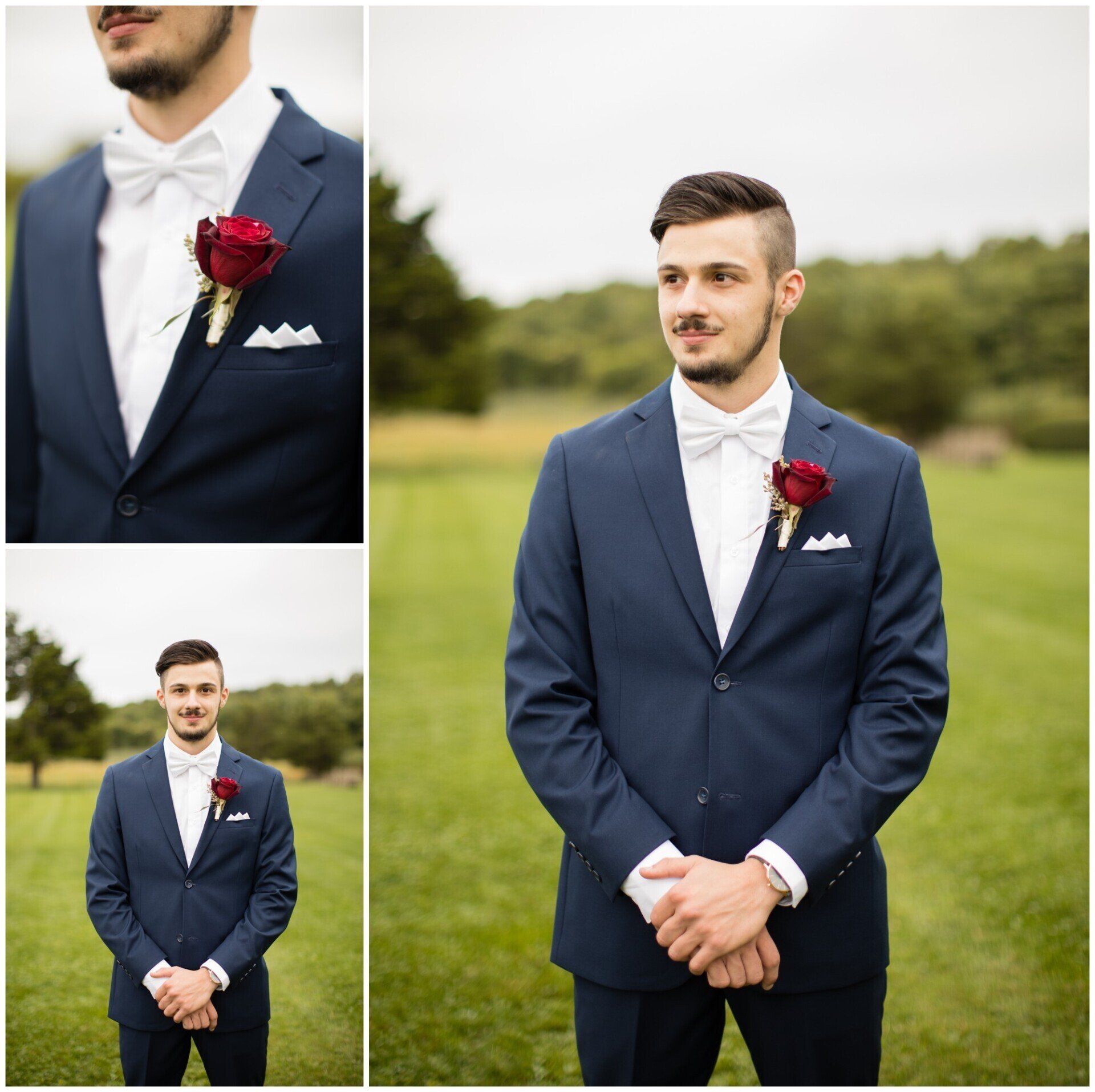 Man in a navy suit with white bow tie and red boutonniere standing outdoors in a grassy field.