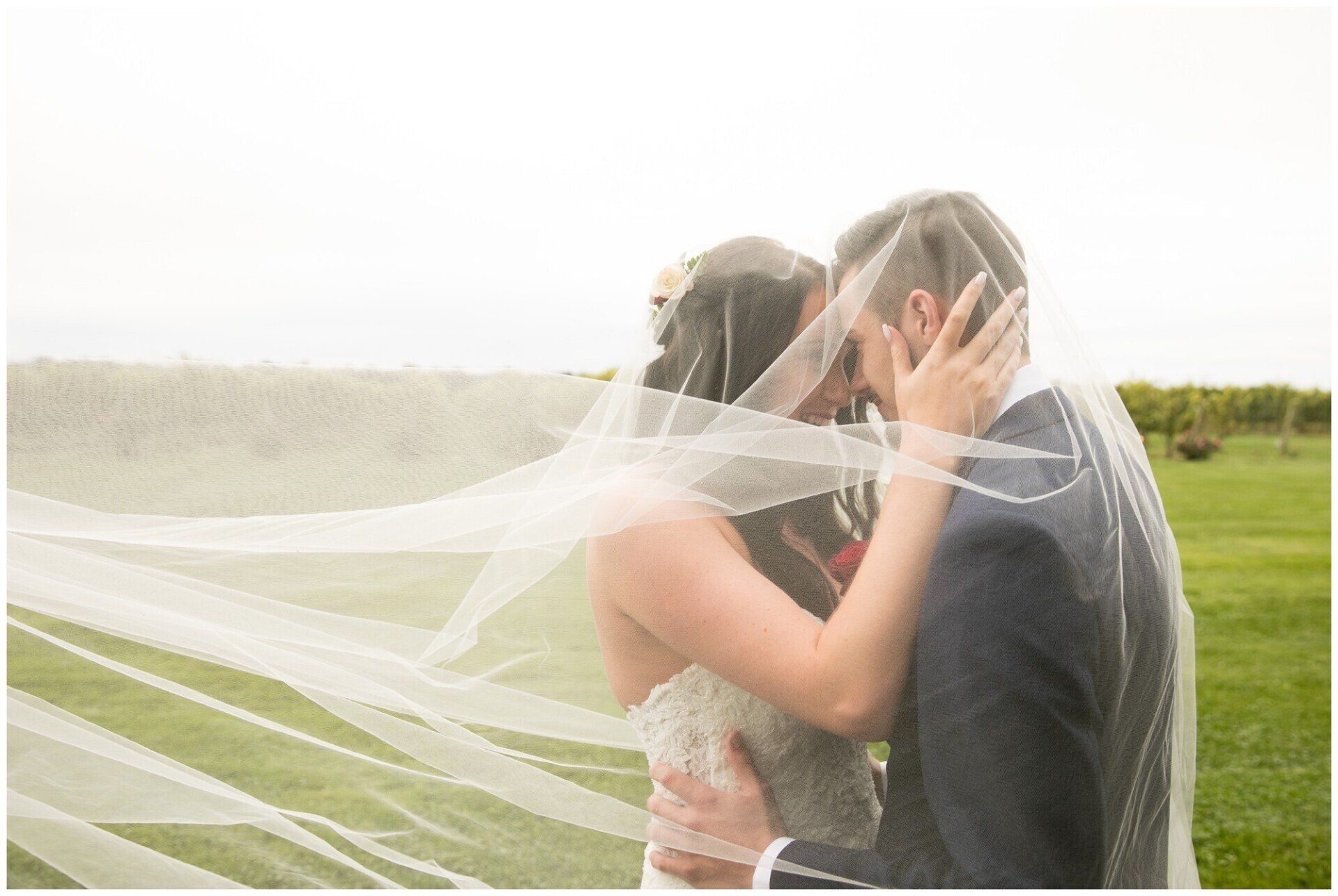 Couple embracing outdoors as a white veil blows across them in the wind