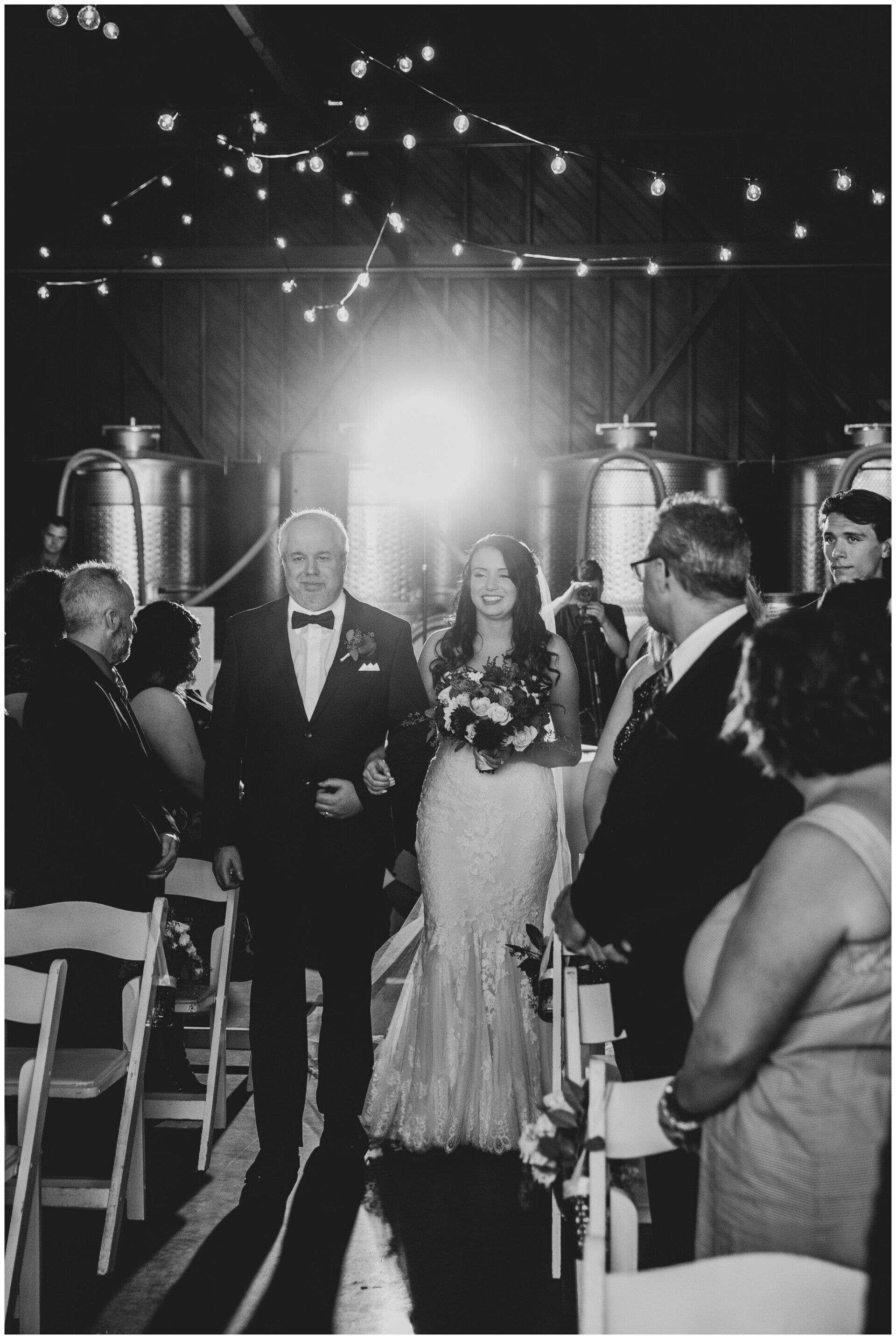 Wedding couple walking down aisle under string lights in a black-and-white photo