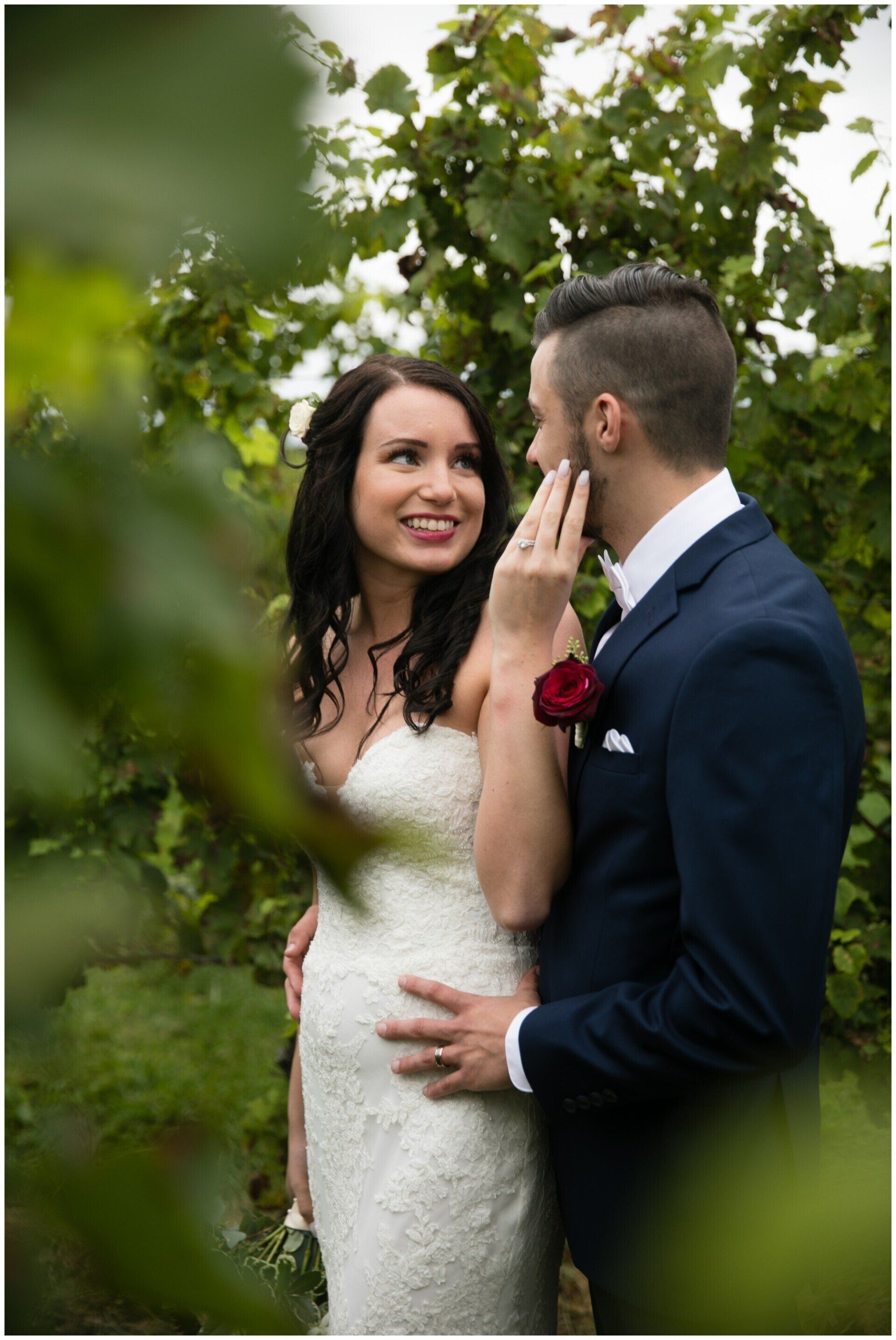Bride and groom in a garden, smiling and embracing among green foliage