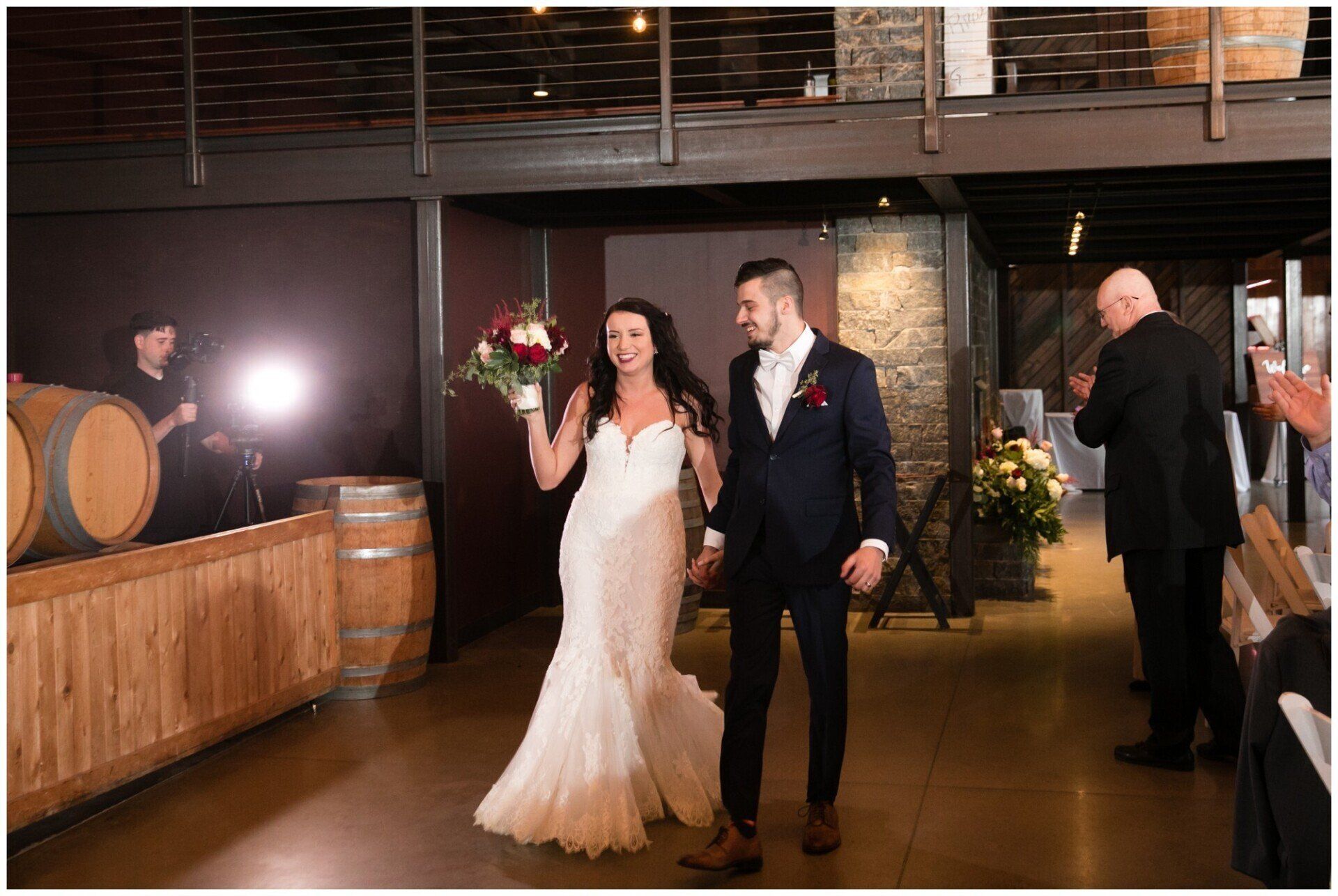 Bride and groom walking into a reception hall, smiling and holding flowers and a drink.