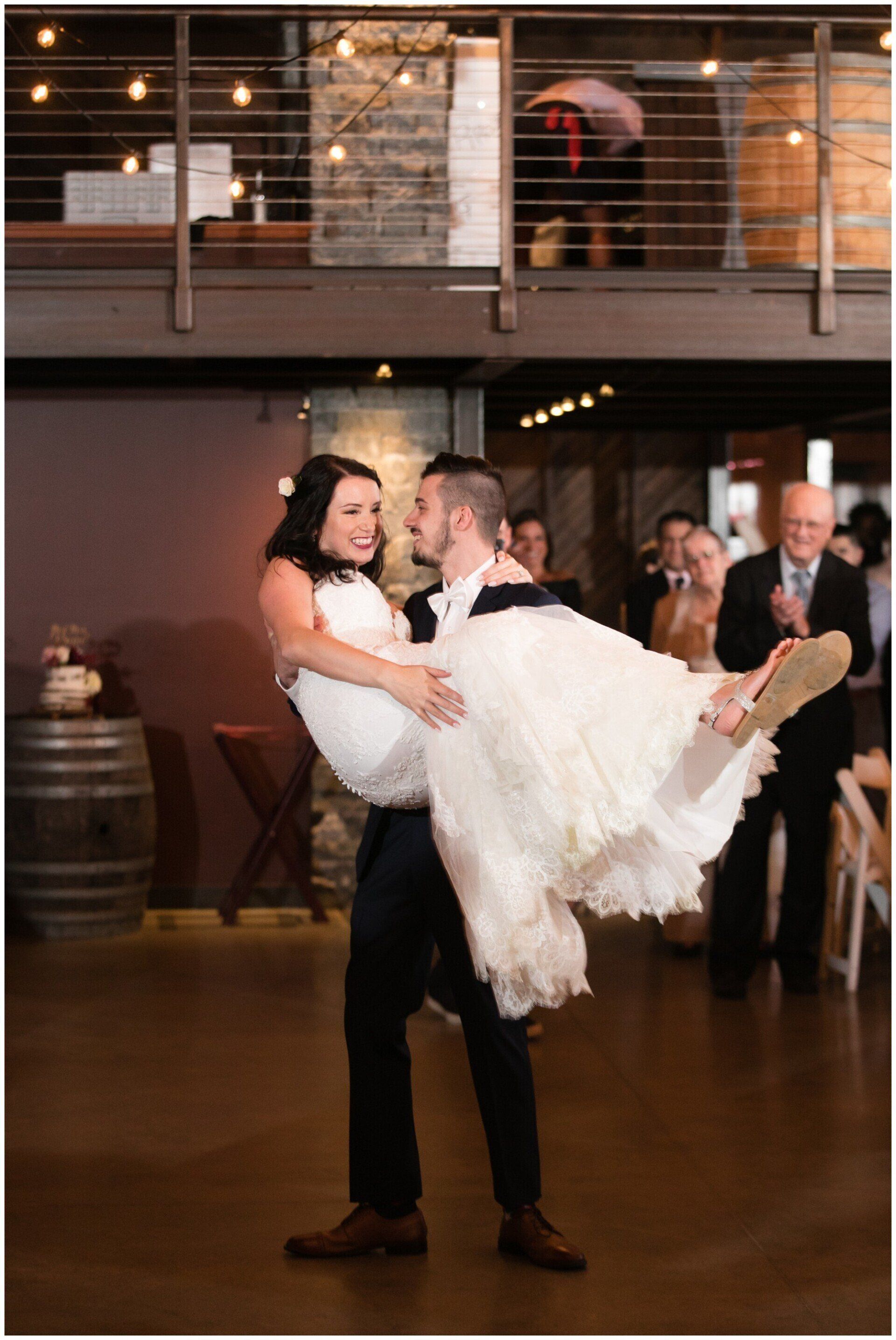 Bride being dipped by partner in a reception hall, guests watching in the background.