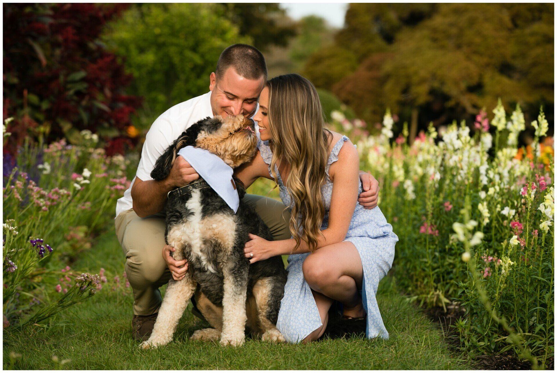 Couple kneeling in a flower garden, hugging a dog with colorful blooms around them