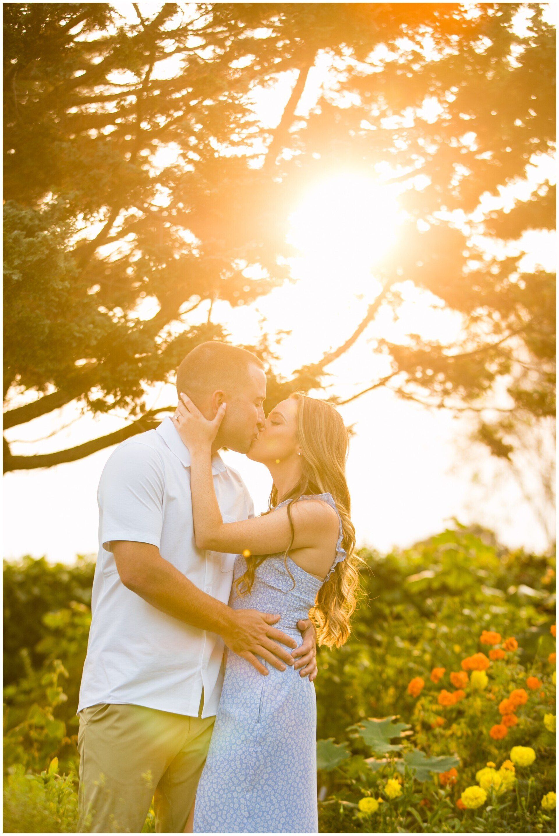 Couple embracing in a sunlit garden with flowers and trees at sunset