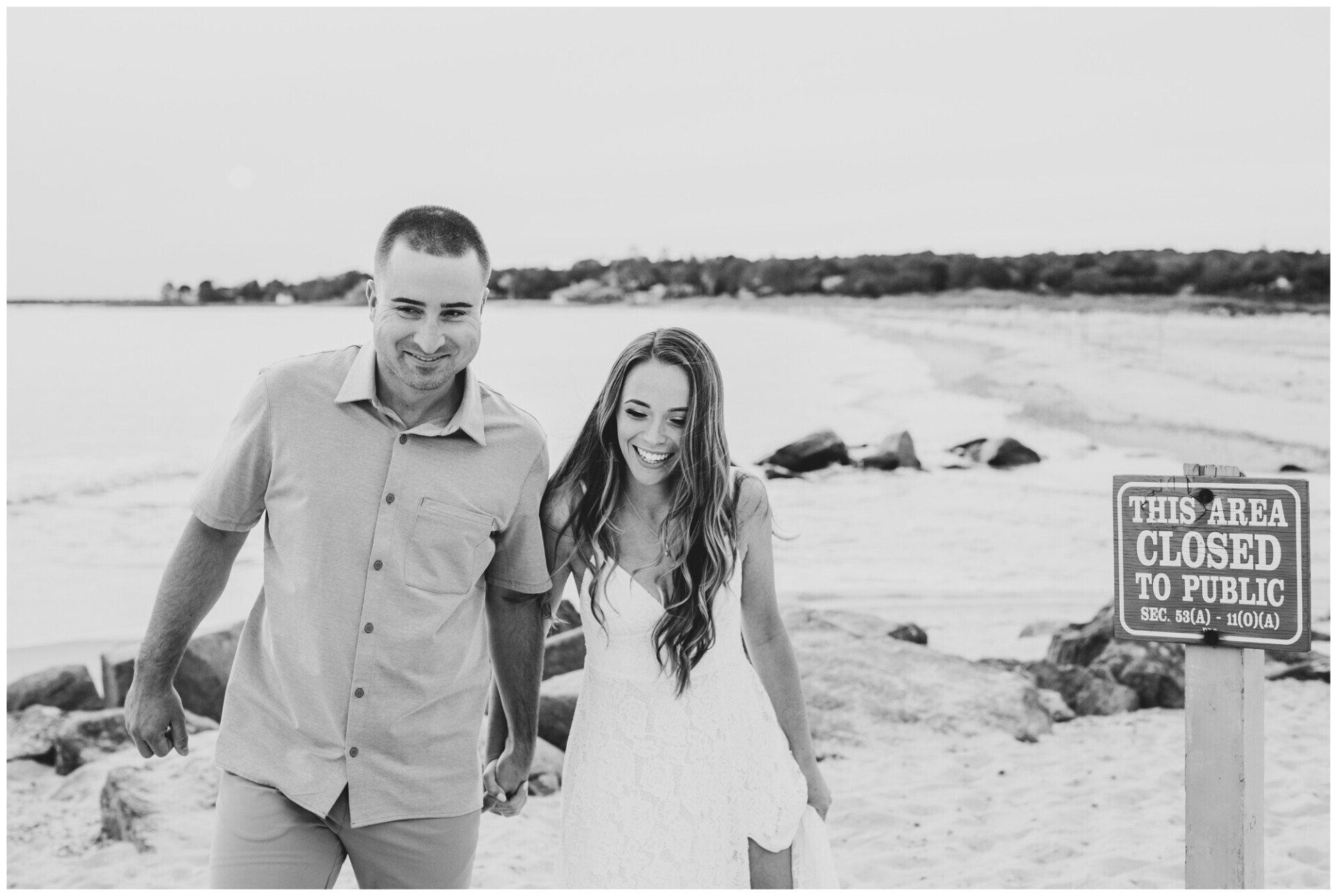 Couple walking on a beach near a sign reading “Closed to Public”