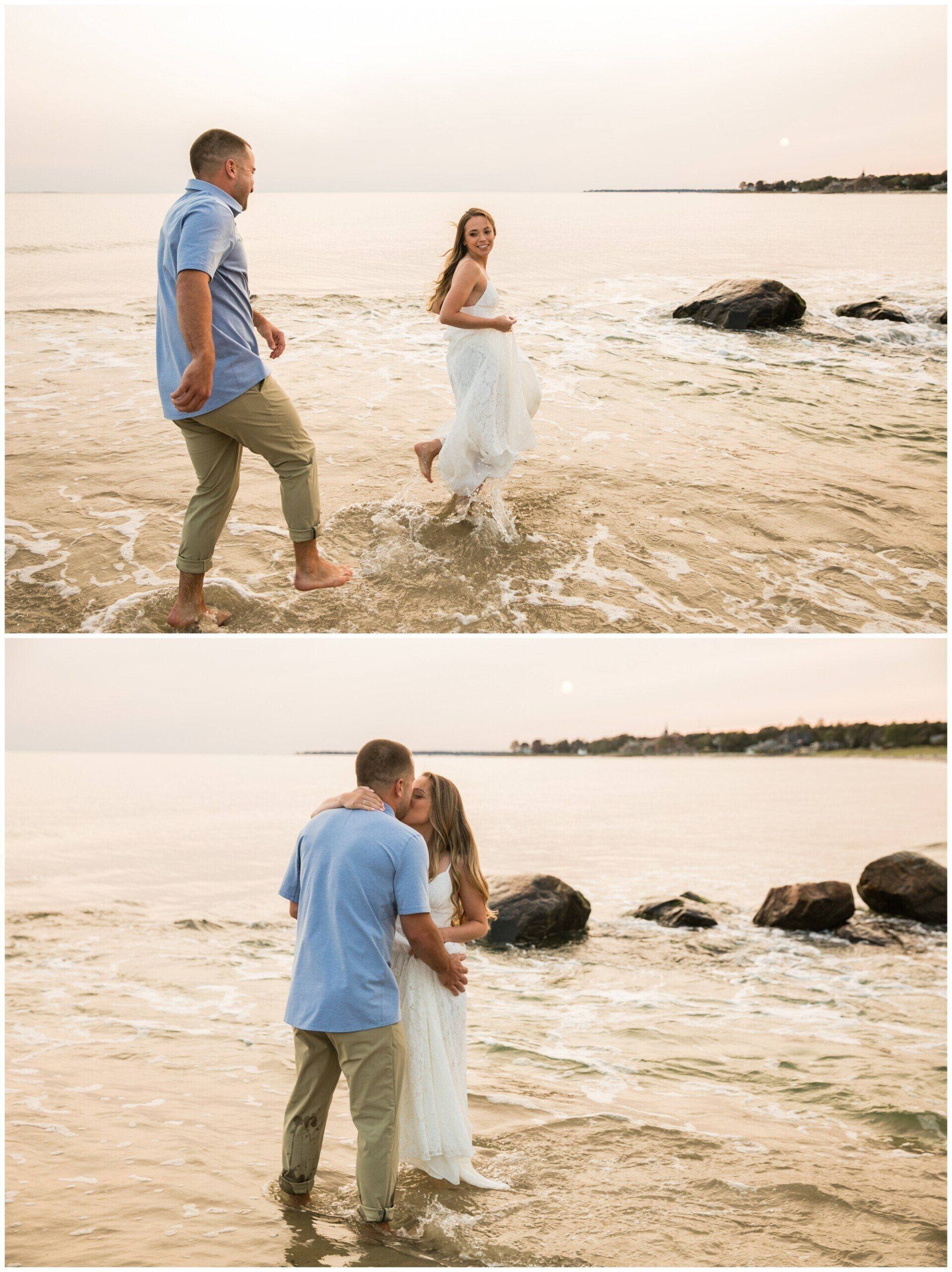 Couple wading in shallow ocean water at sunset, embracing on a rocky beach.