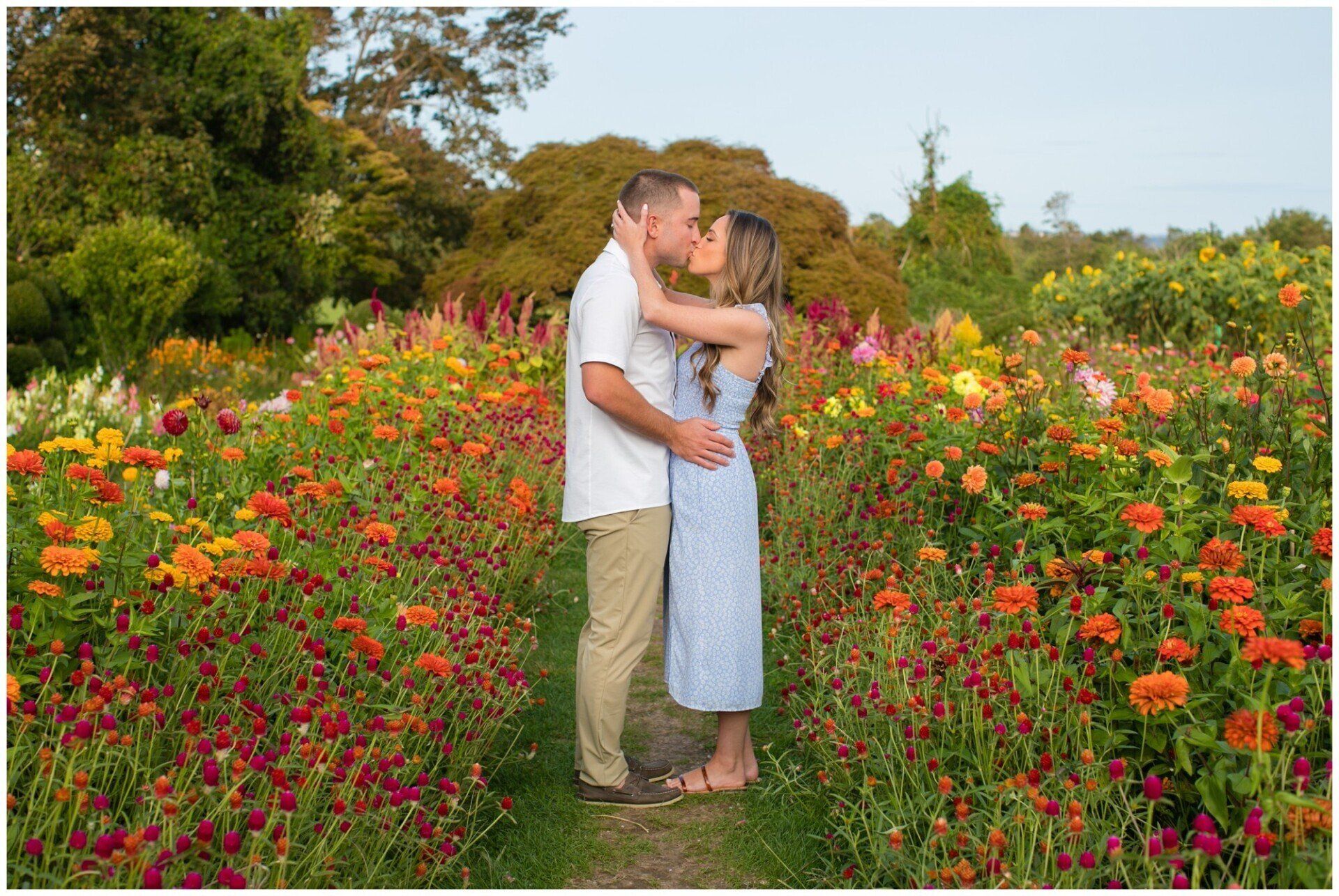 Couple embracing in a colorful flower garden with trees and greenery behind them