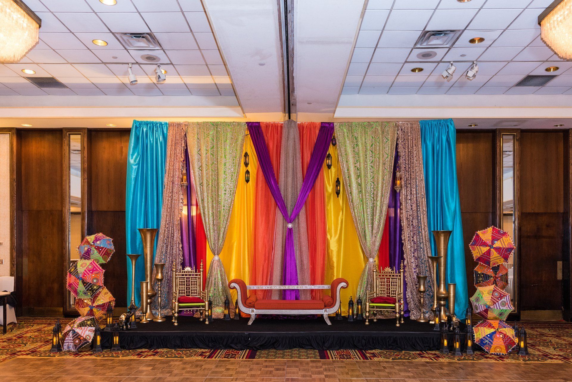 Decorated stage with colorful drapes, chairs, and floral arrangements at an event venue