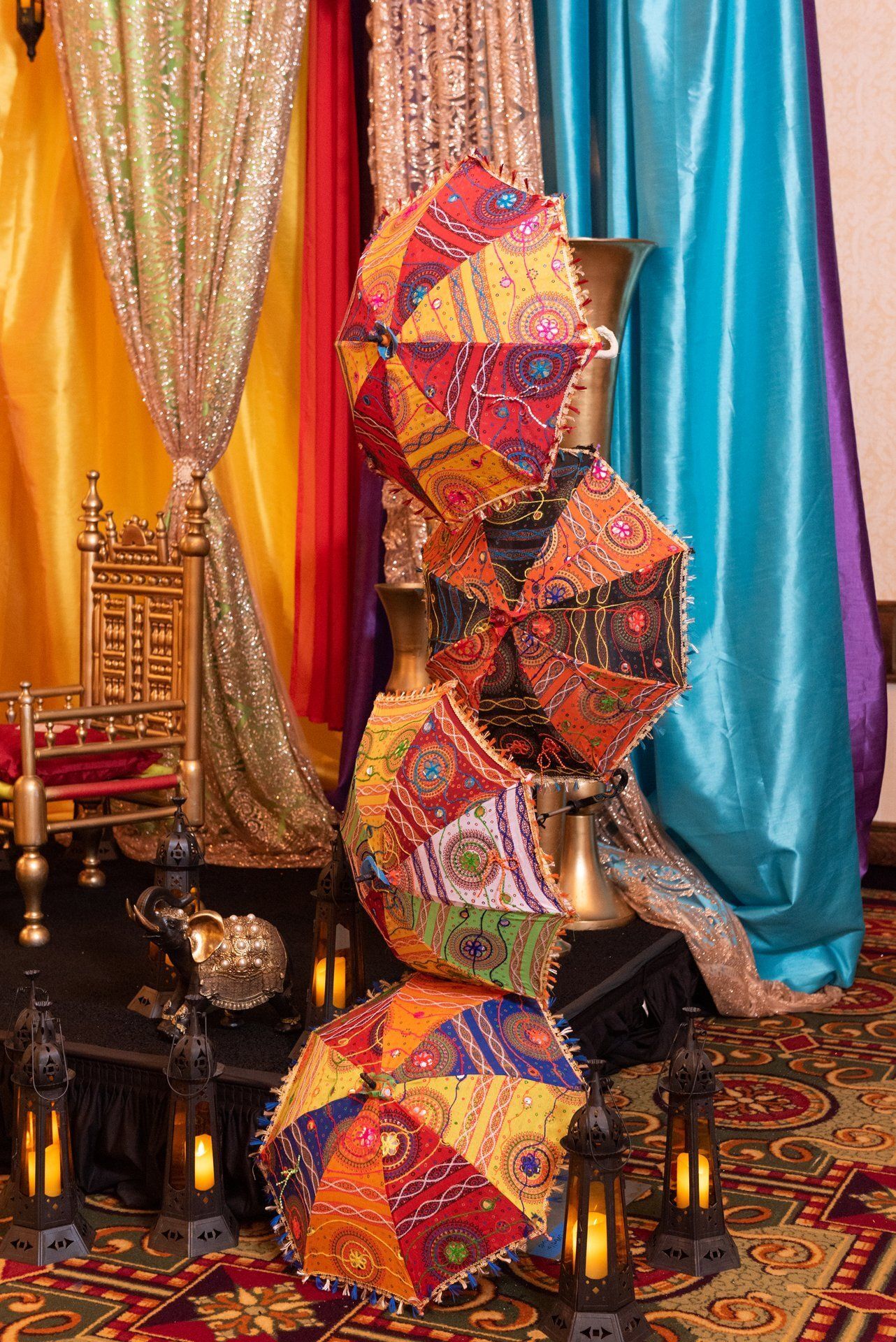 Colorful geometric sculpture made of stacked umbrellas against gold, teal, and red drapes in an ornate room
