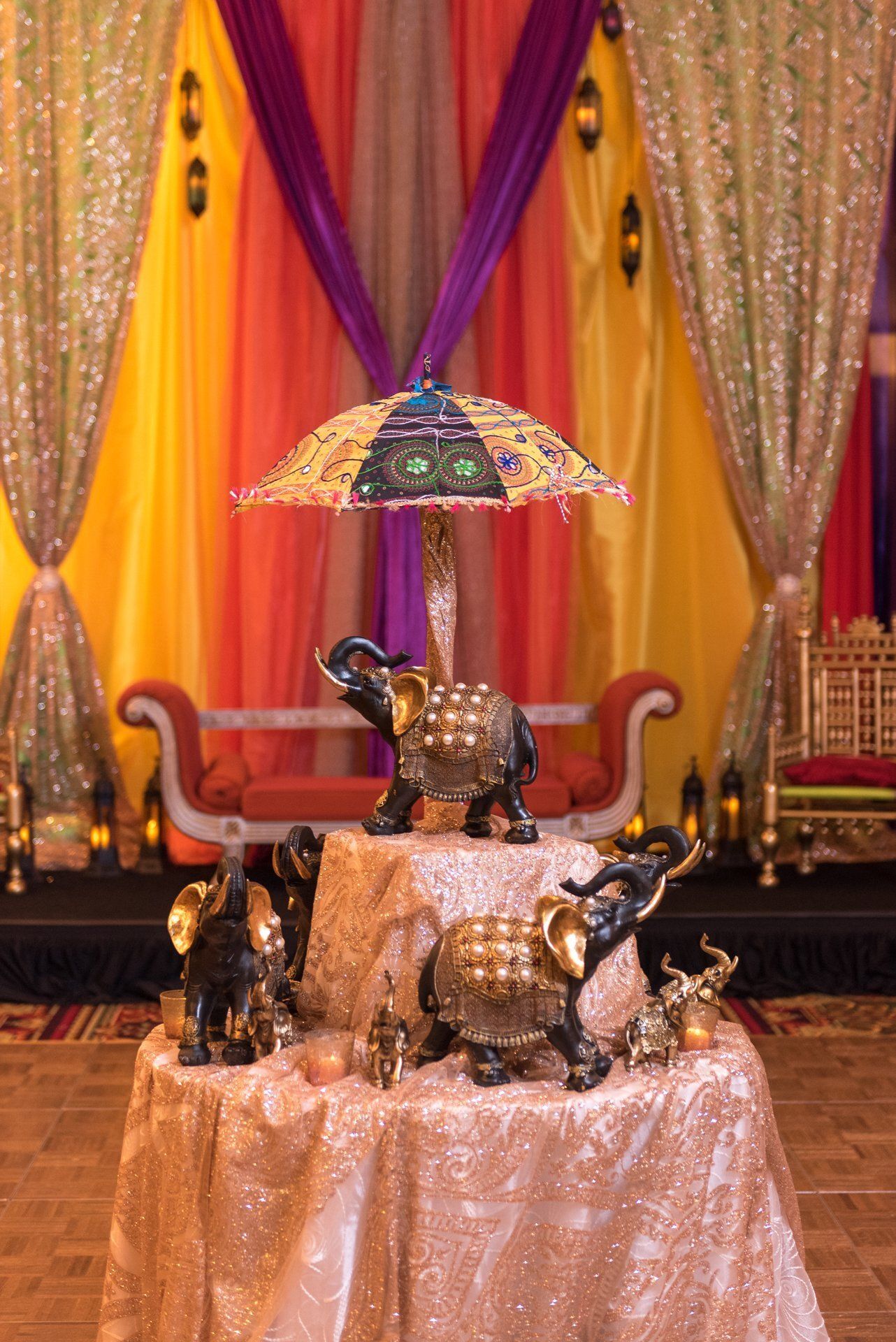 Decorative elephant figurines under a jeweled umbrella on a glittering draped stage backdrop