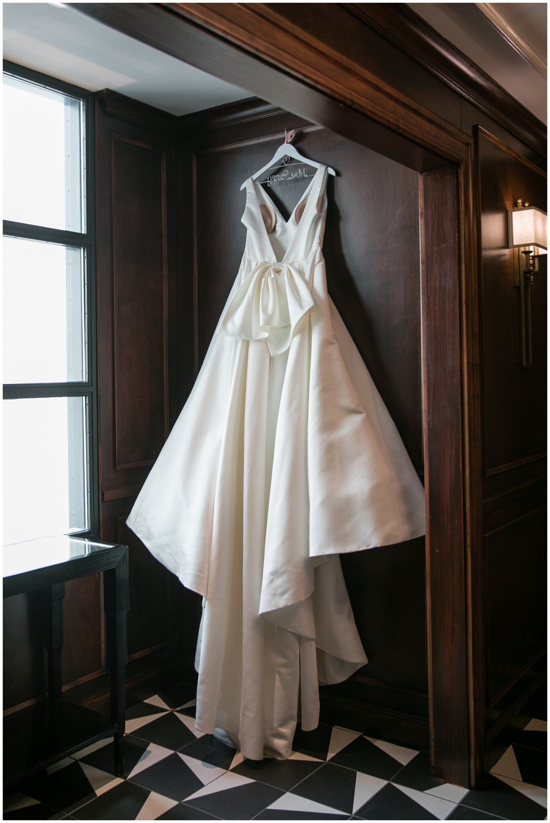 White wedding dress hanging in a wooden doorway beside a window and wall sconce