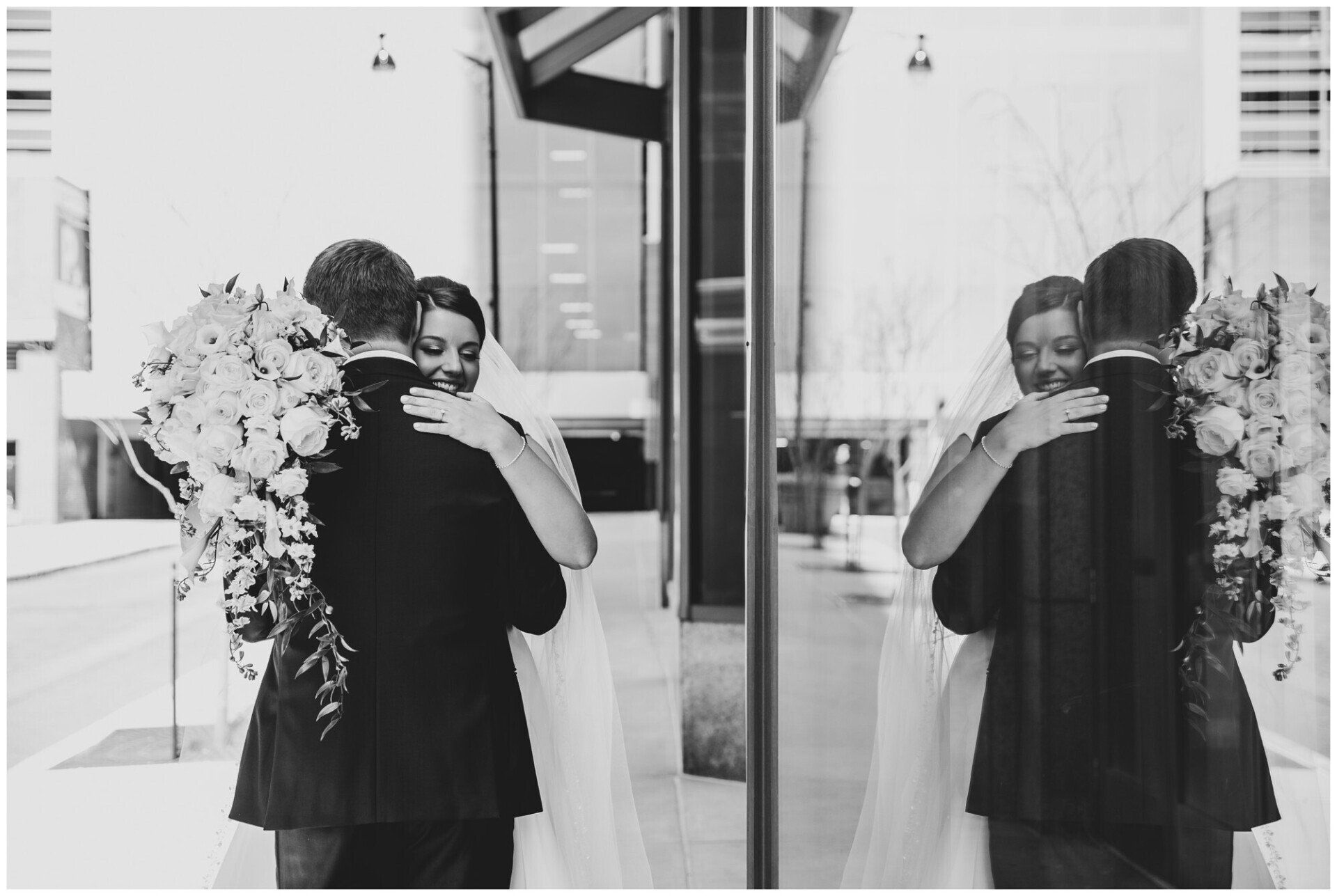 Person in black dress holds bouquet while embracing another in a mirrored doorway.
