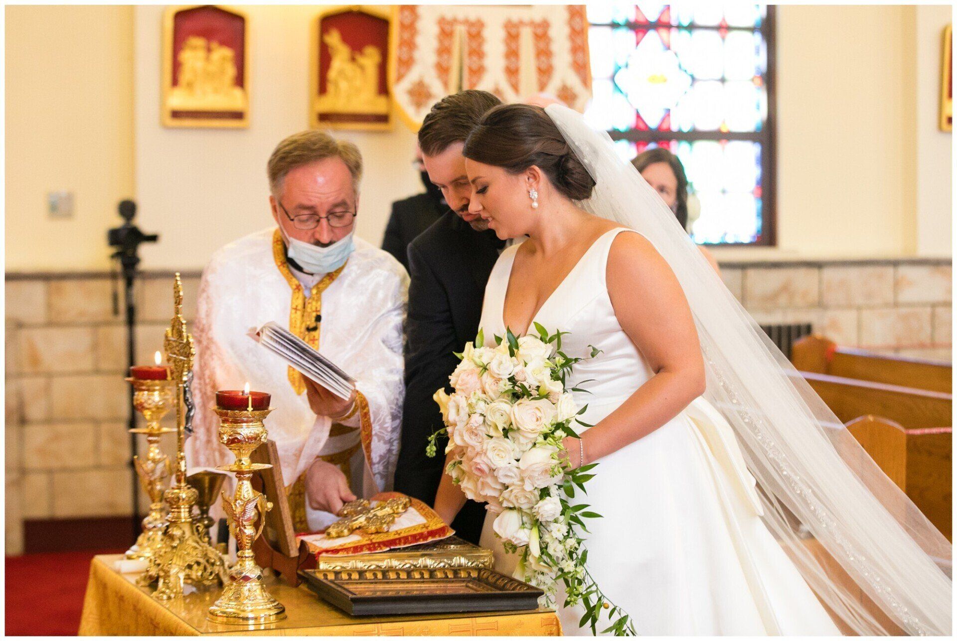 Bride signing marriage documents in a church, with an officiant and altar decorations nearby