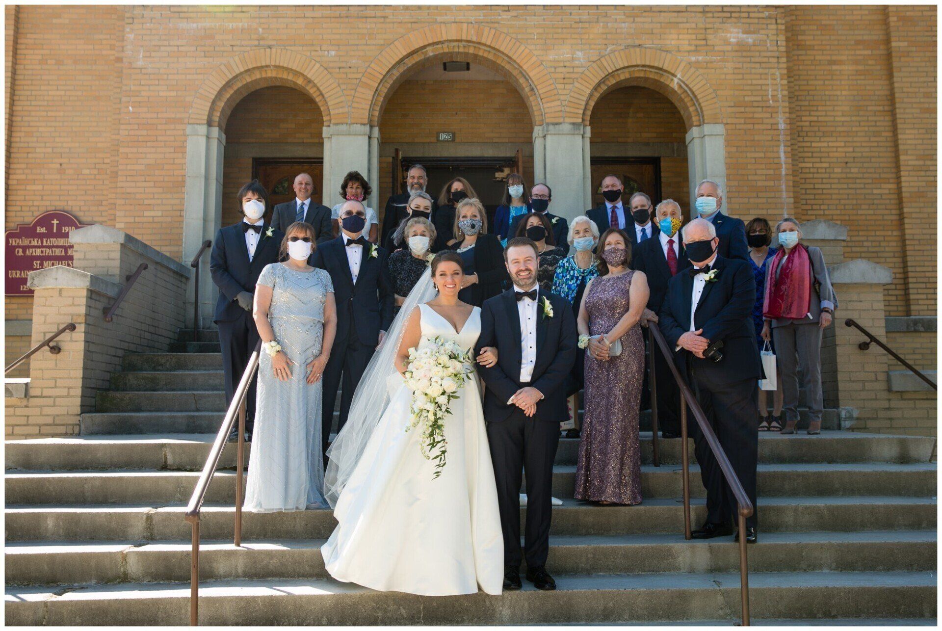 Wedding party posing on church steps, with bride, groom, and guests in formal attire