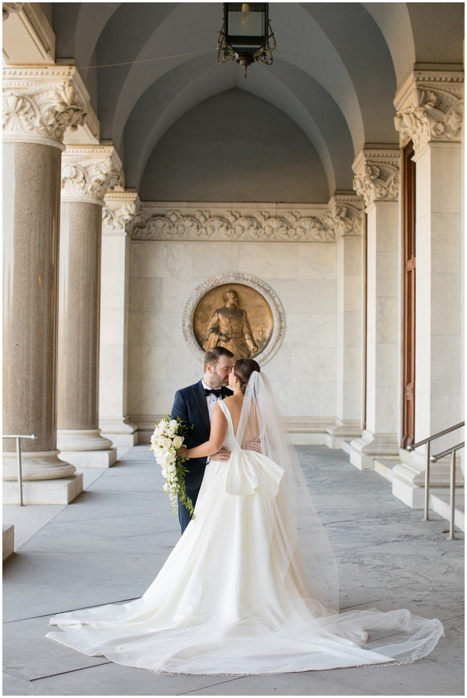 Bride and groom embracing in a grand arched hallway, bride in a long white gown
