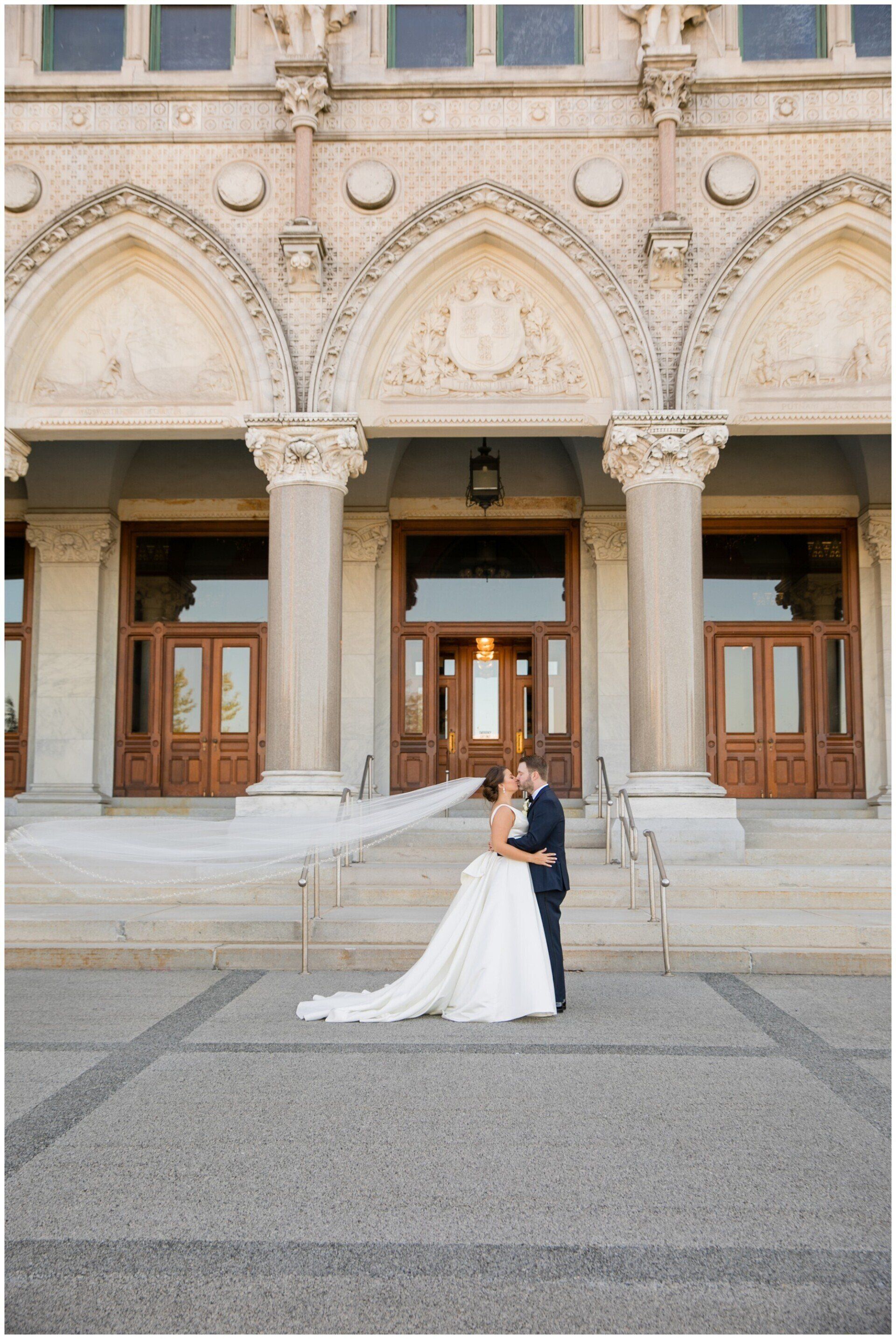 Bride and groom posing in front of an ornate stone building with arched entrances