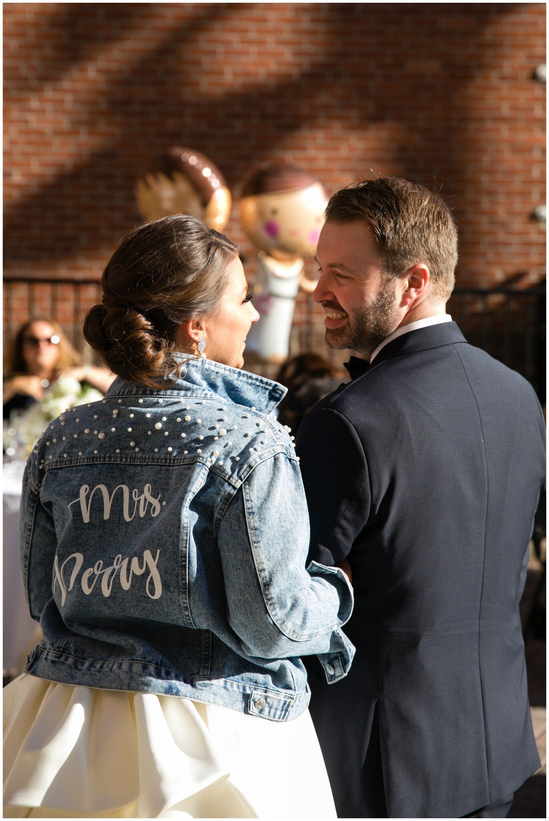 Couple facing each other at an outdoor event, woman in denim jacket with “I’m a …” embroidered on the back.