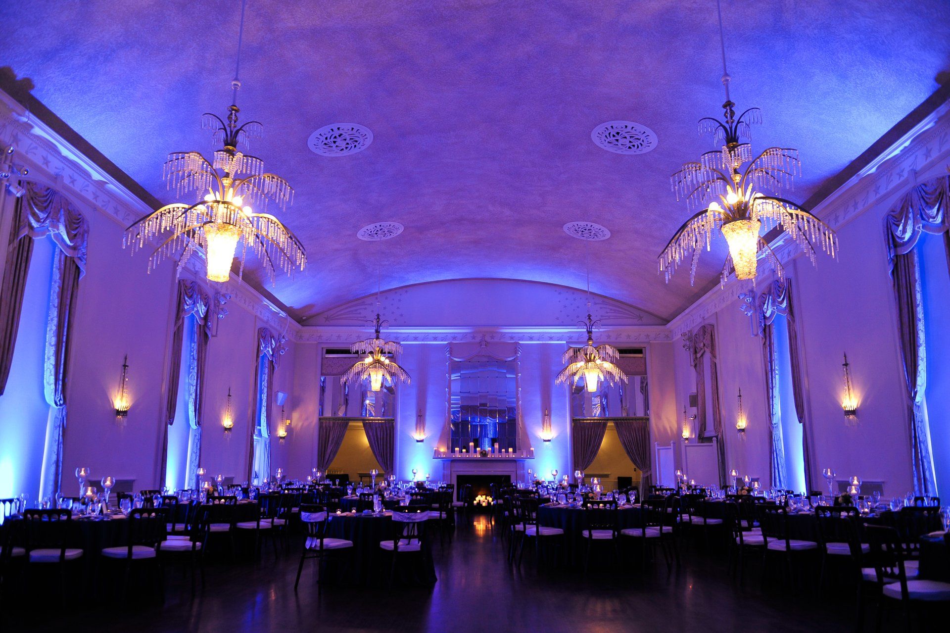Elegant banquet hall with blue lighting, chandeliers, and long dining tables set for an event