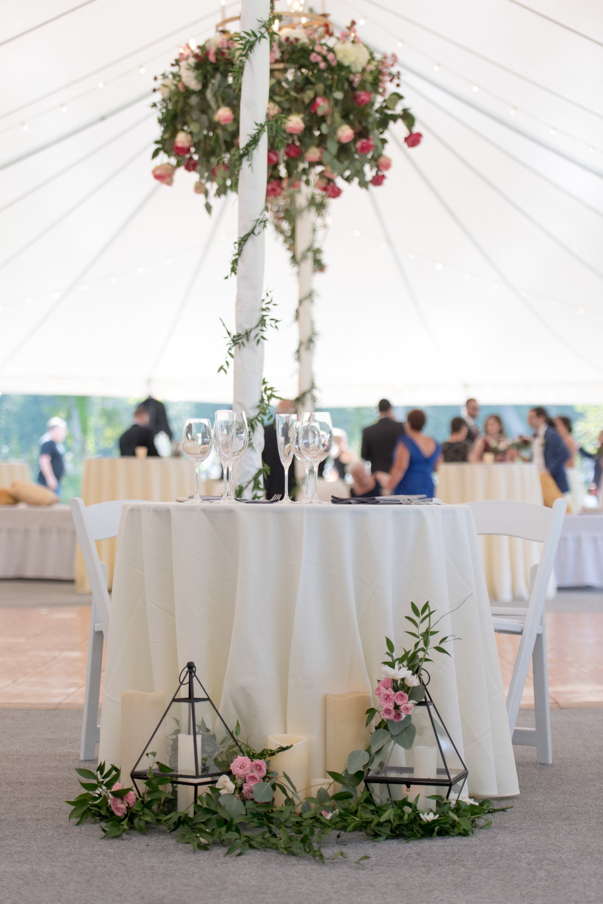 Decorated wedding reception table under a white tent with floral centerpiece and greenery accents