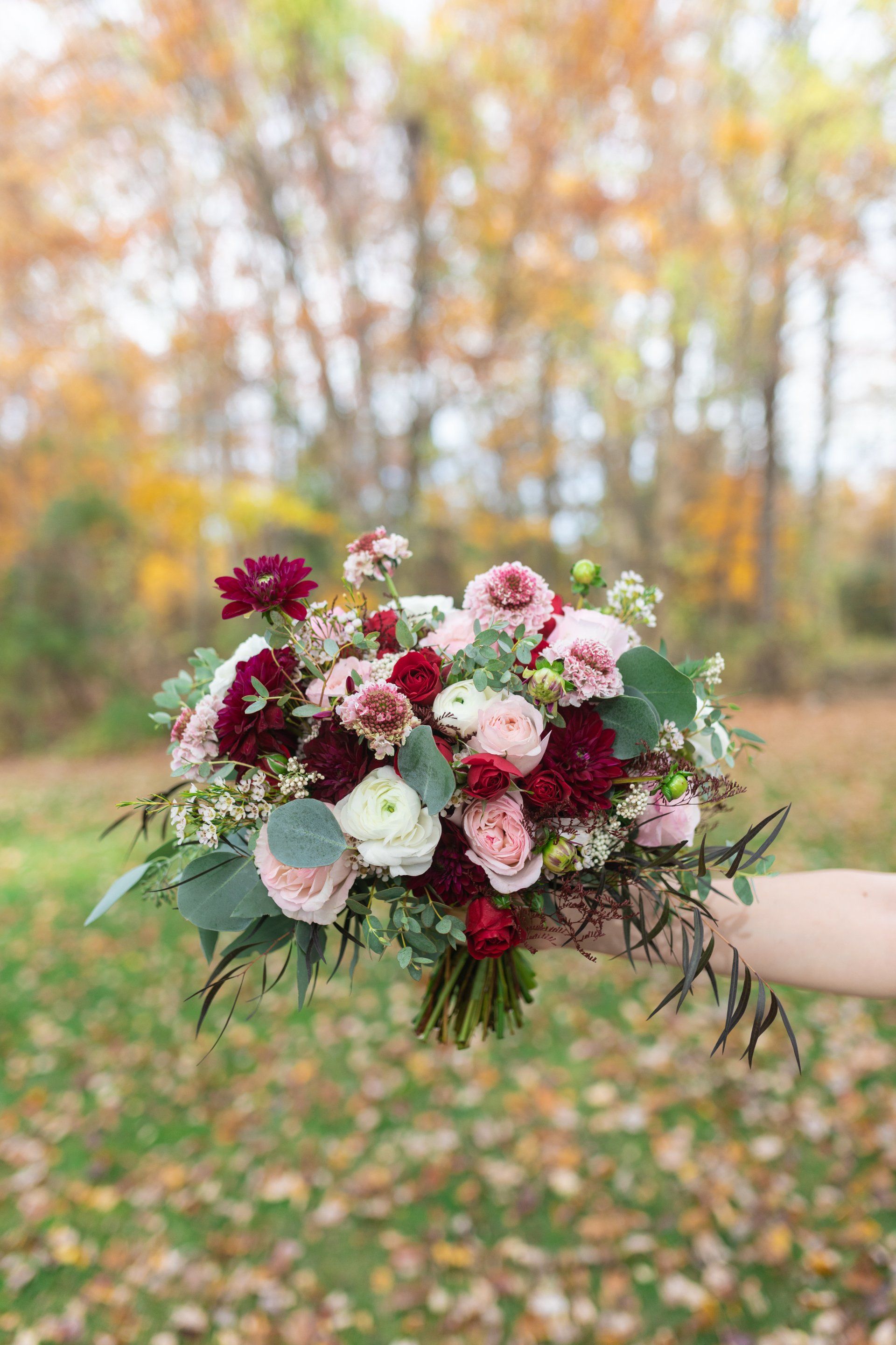 Bouquet of pink, white, and burgundy flowers held outdoors against a blurred autumn background