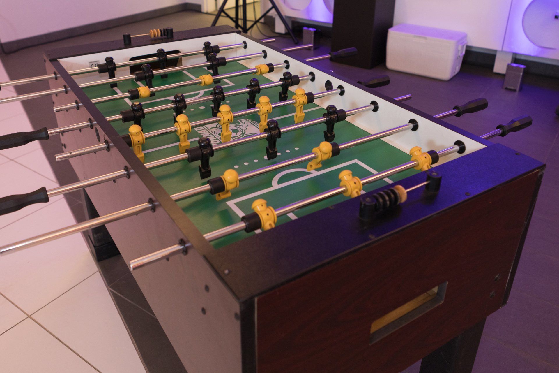 Foosball table with green field and yellow and black players in a game room
