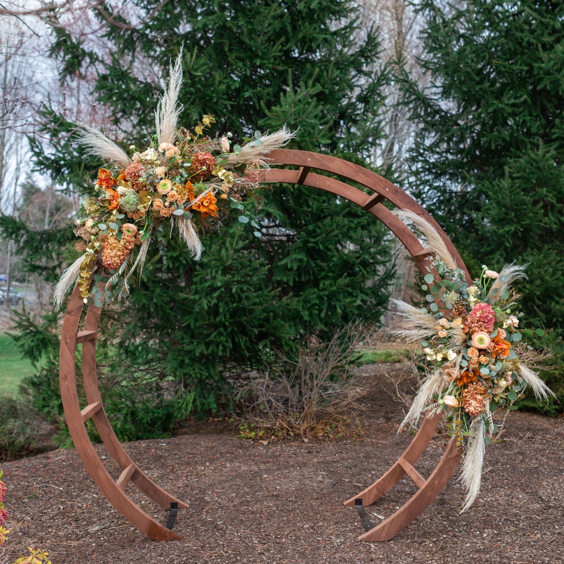 Rustic circular floral arch with orange and white arrangements in an outdoor wooded setting