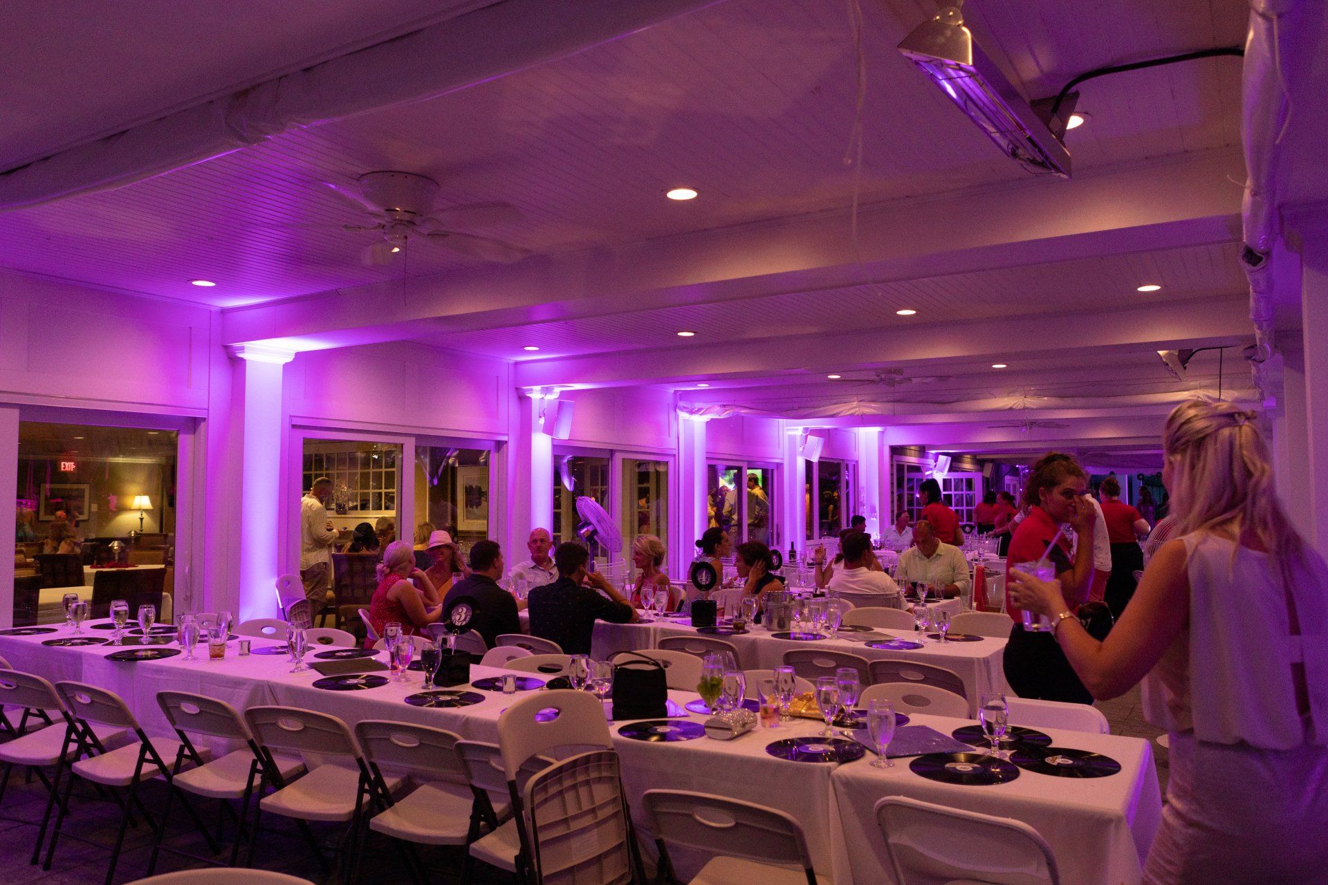 Purple-lit banquet hall with guests dining at round tables and a woman taking a photo with a phone