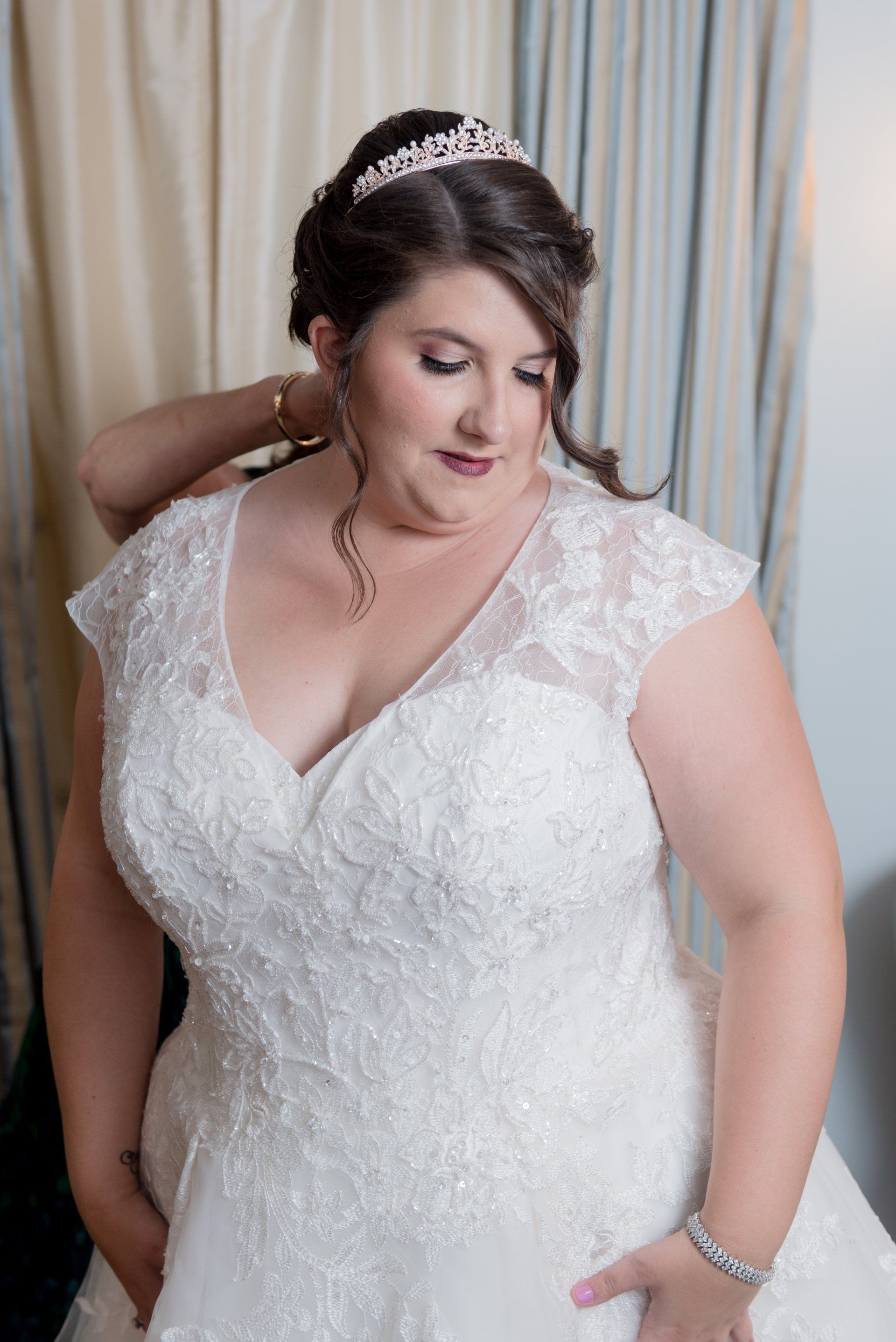 Bride in a white lace wedding dress posing indoors with a tiara and veil