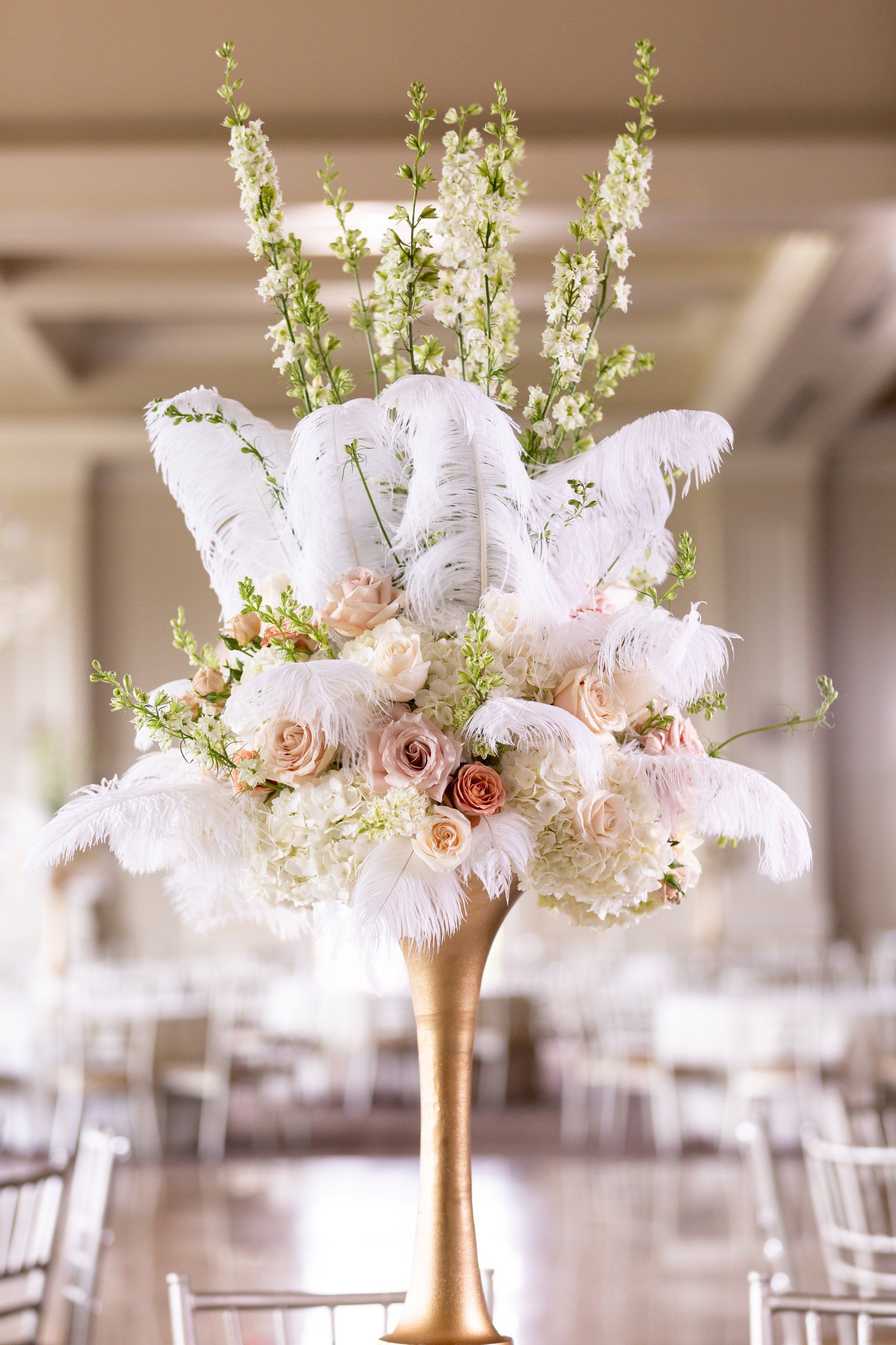 Tall white and blush floral centerpiece in a gold vase at a wedding reception table