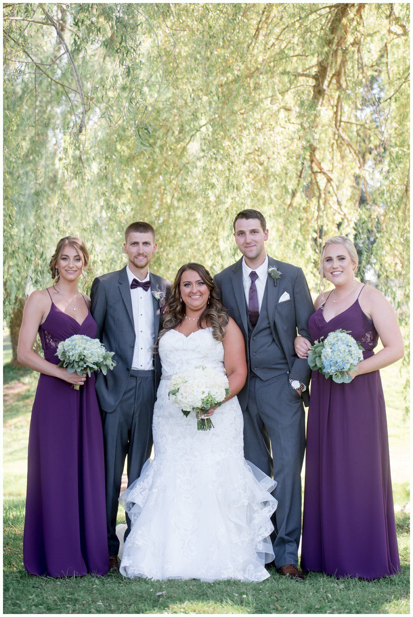 Wedding party posing outdoors beneath hanging willow branches.