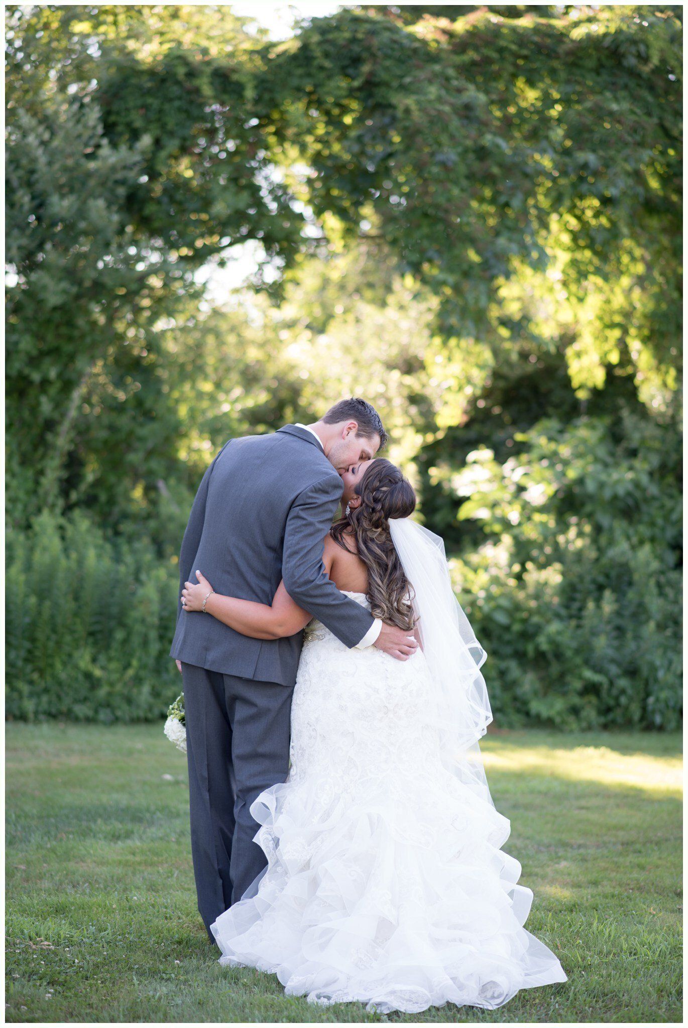 Bride and groom embracing outdoors under trees on a grassy lawn