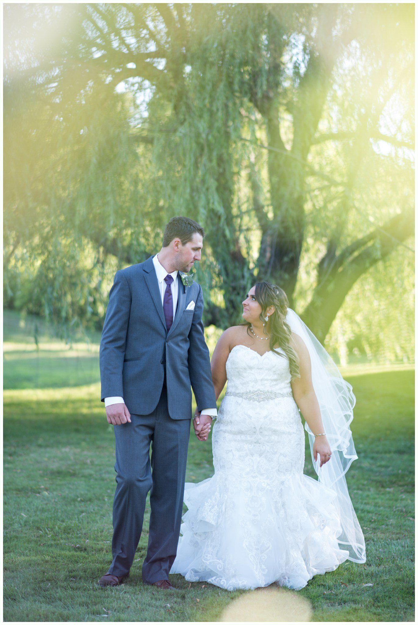 Bride and groom standing together in wedding attire in a sunlit outdoor park