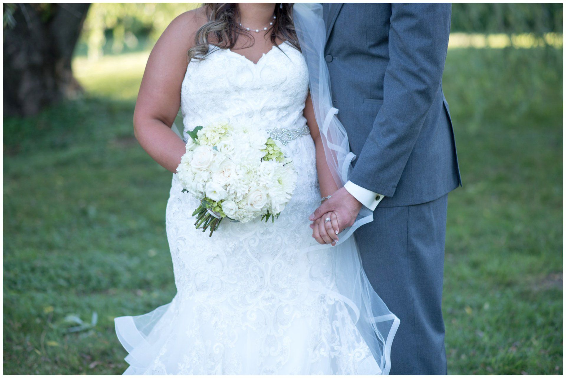Bride and groom holding hands outdoors, bride in white lace gown with bouquet